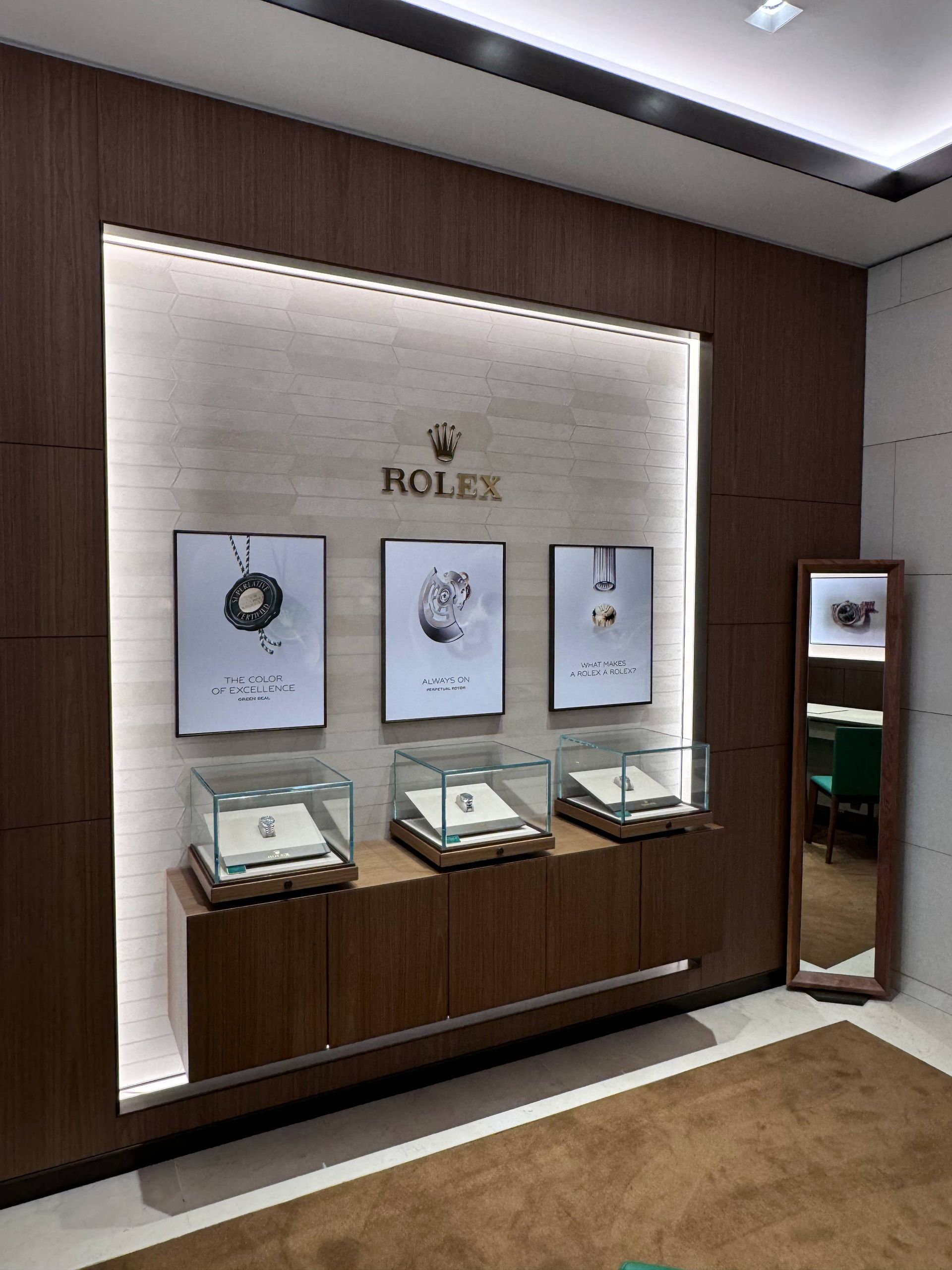 A Rolex display in a boutique featuring three framed posters above individual glass jewelry cases on a wooden console.