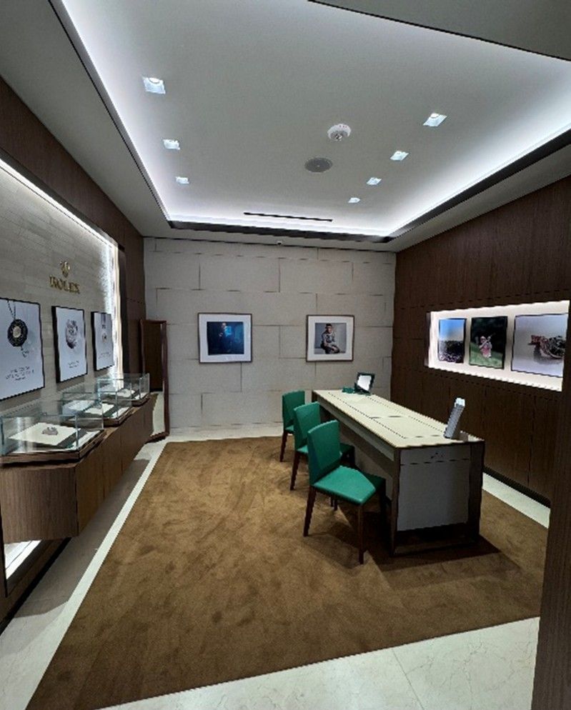 A modern showroom with a desk, two teal chairs, wood paneling, and framed artwork on the walls.