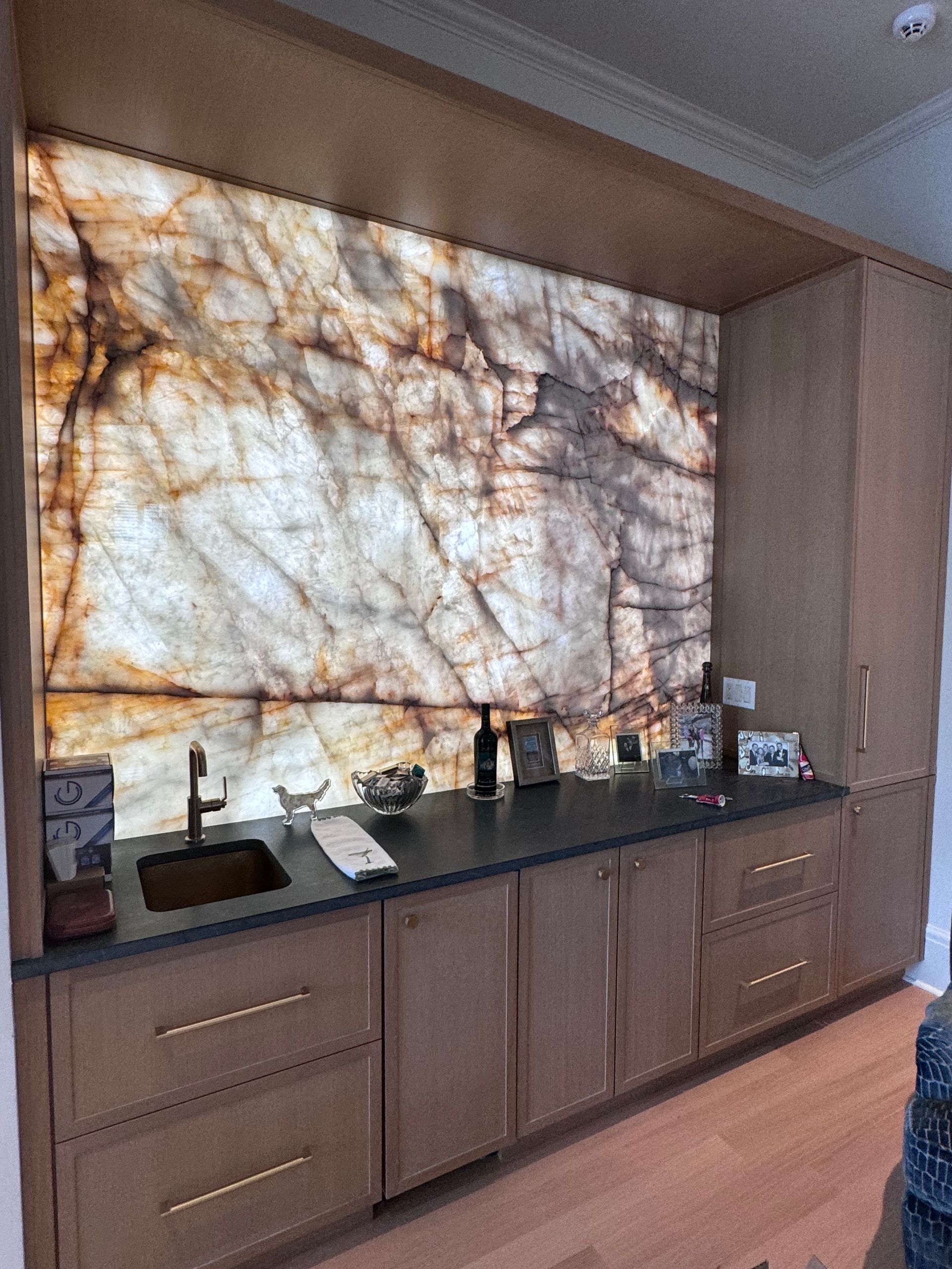 Backlit marble countertop bar with sink, drawers, and cabinet, set in a wood frame.
