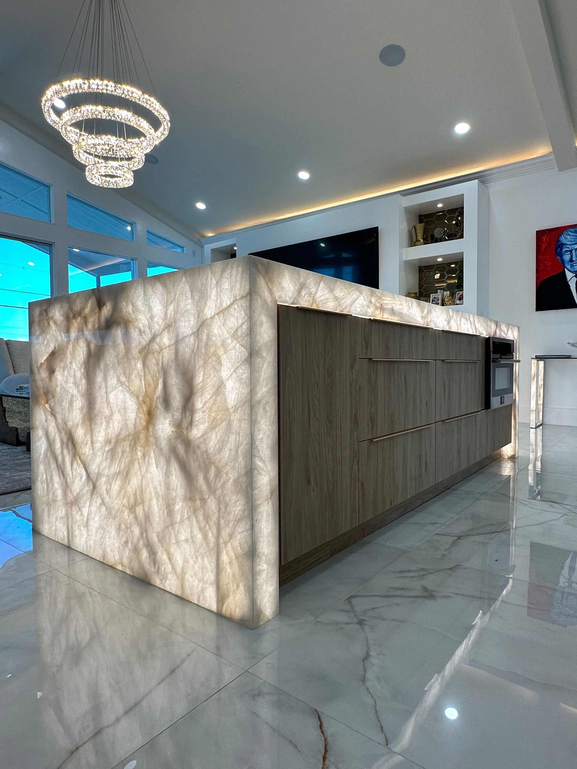 Modern kitchen island with lit, veined stone sides, wood cabinetry, and marble floor.