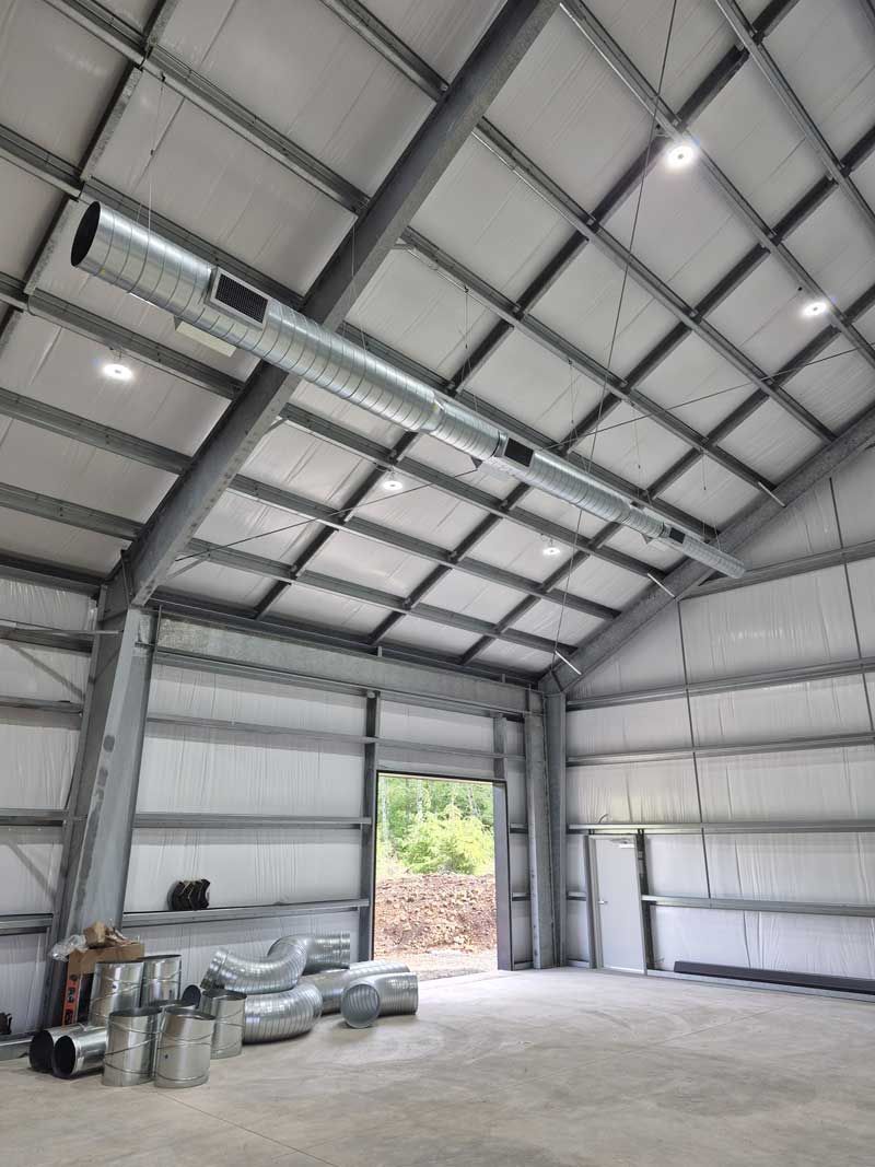 Interior view of a metal building with exposed beams, ventilation, and an open doorway.
