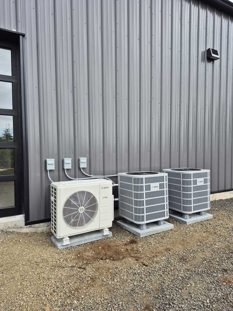 Three AC units next to a building with metal siding; electrical boxes are also visible.