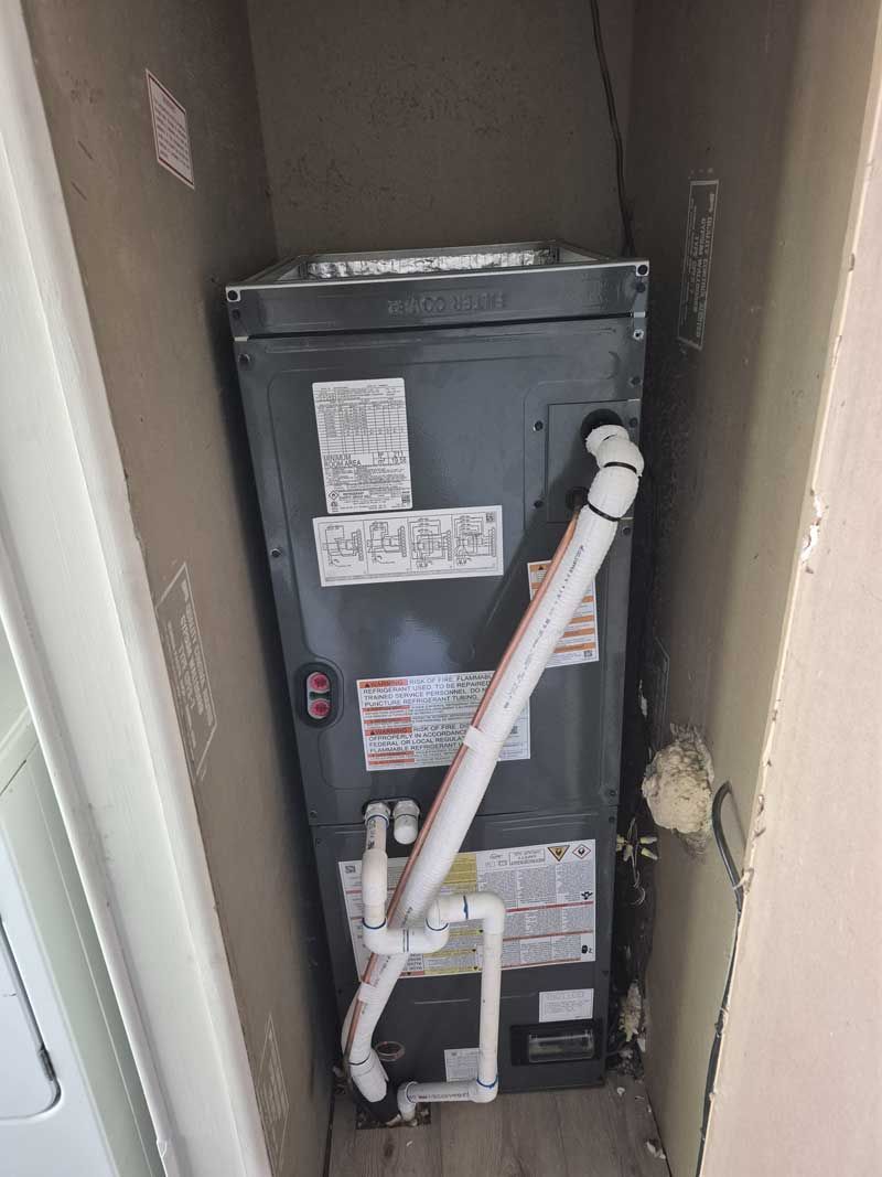 A tall, gray HVAC unit in a closet with white PVC piping.