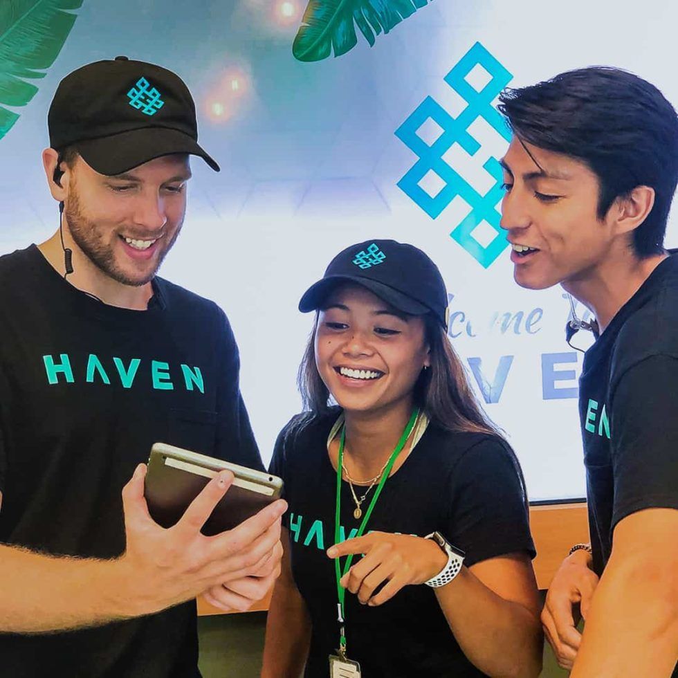 Three people wearing Haven shirts and hats looking at a tablet, smiling.