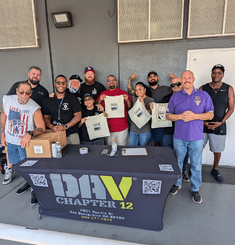 Group of people with DAV Chapter 12 banner, holding bags, posing outdoors.