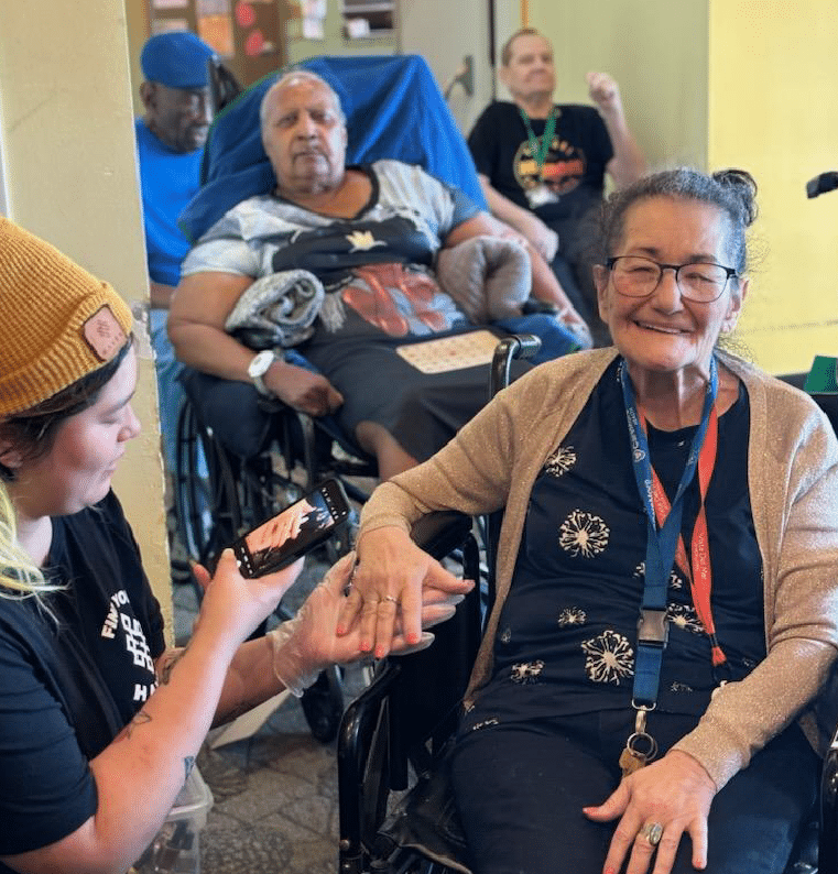 Woman receiving hand treatment, smiling, with others in wheelchairs nearby.