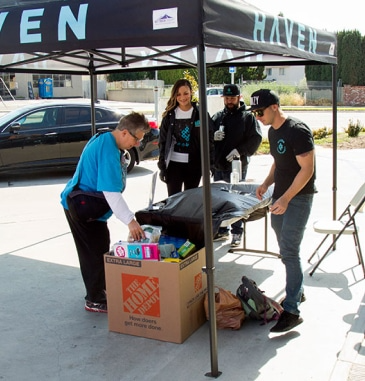 People at a Haven tent, unpacking items from a Home Depot box. Donations being distributed outside.