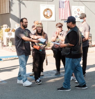 People exchanging papers outdoors, American flag in background.