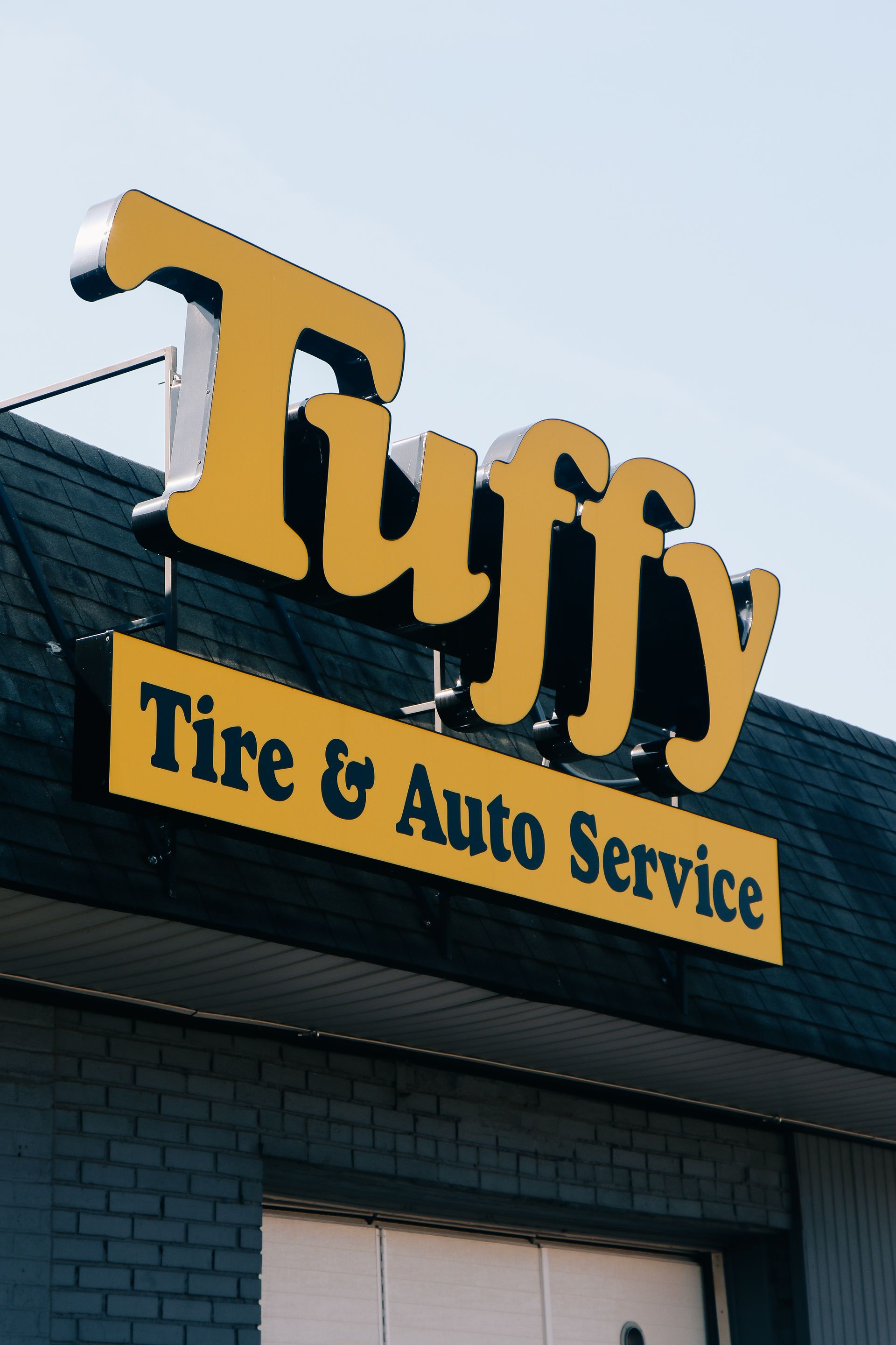 Tuffy Tire & Auto Service sign in yellow on a building with a dark roof.