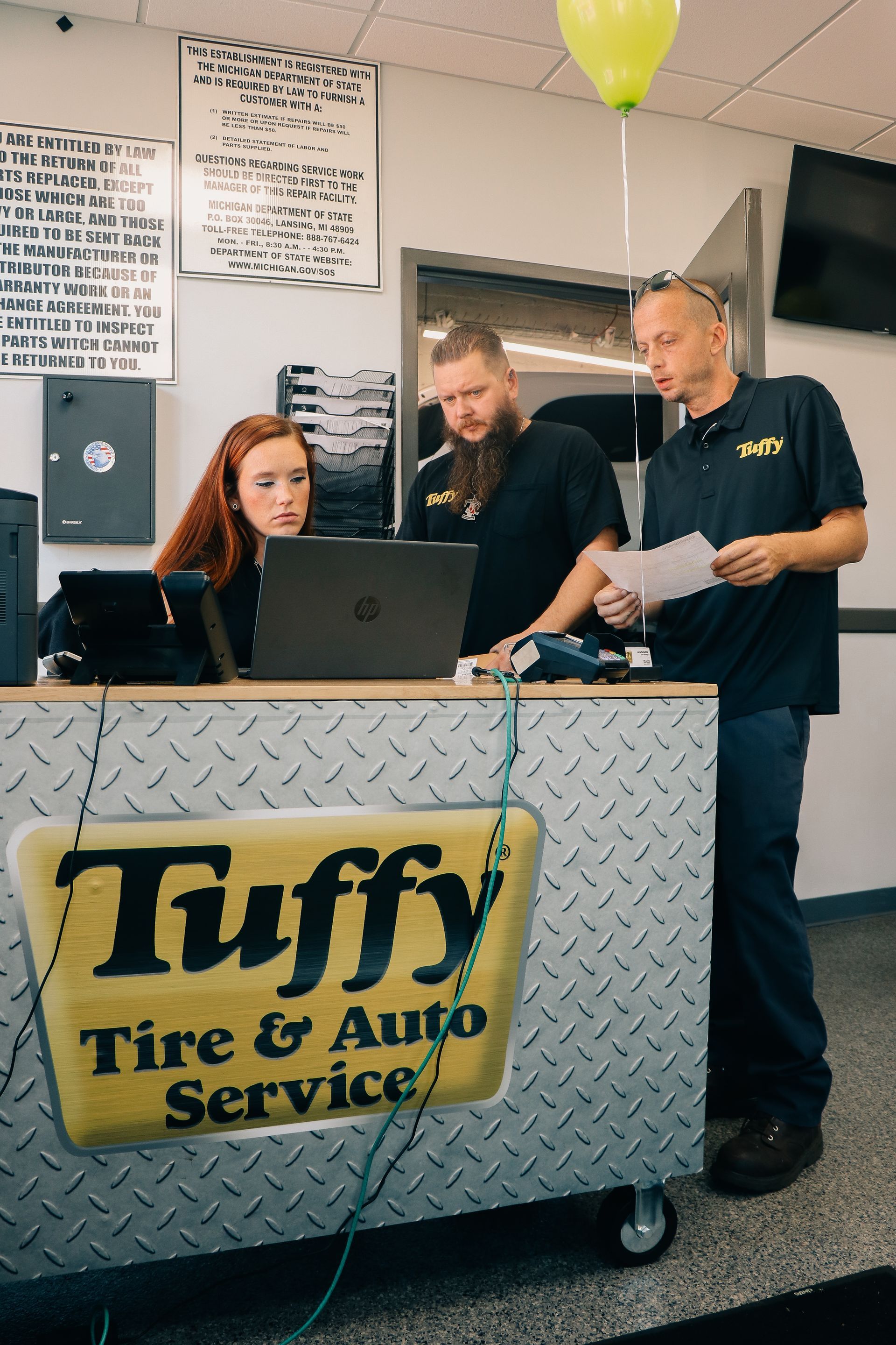 Three people at a Tuffy Tire & Auto Service counter looking at a laptop and paperwork.