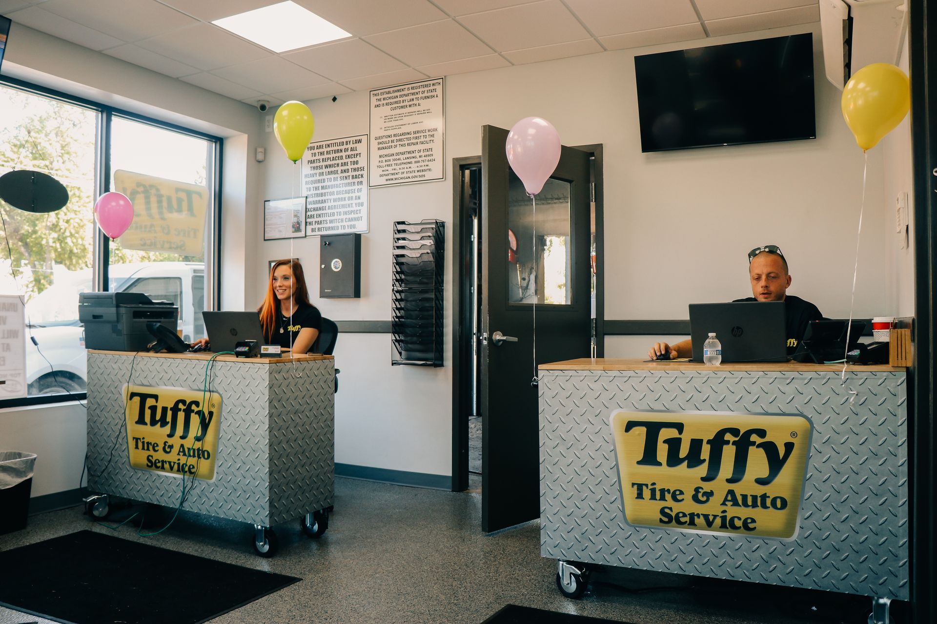 Two people at Tuffy Tire & Auto Service reception desks, with balloons.