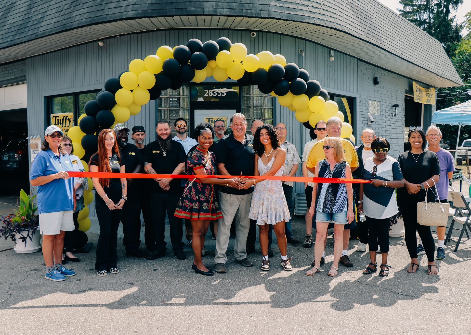 Group of people celebrating outside Tuffy Tire & Auto Service. They are pointing upward.