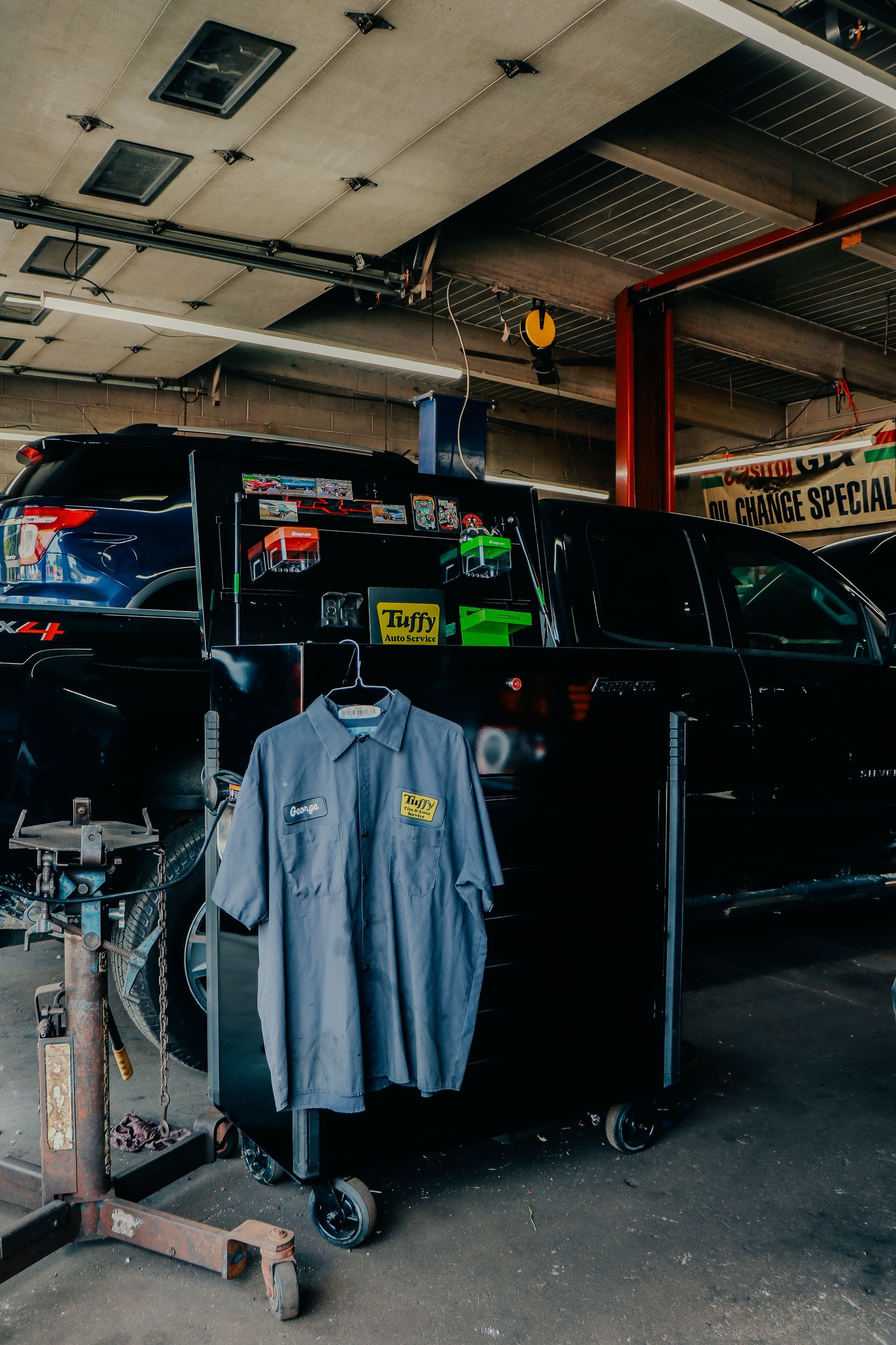 Mechanic's shirt hangs on a toolbox in a car repair shop with a black vehicle in the background.