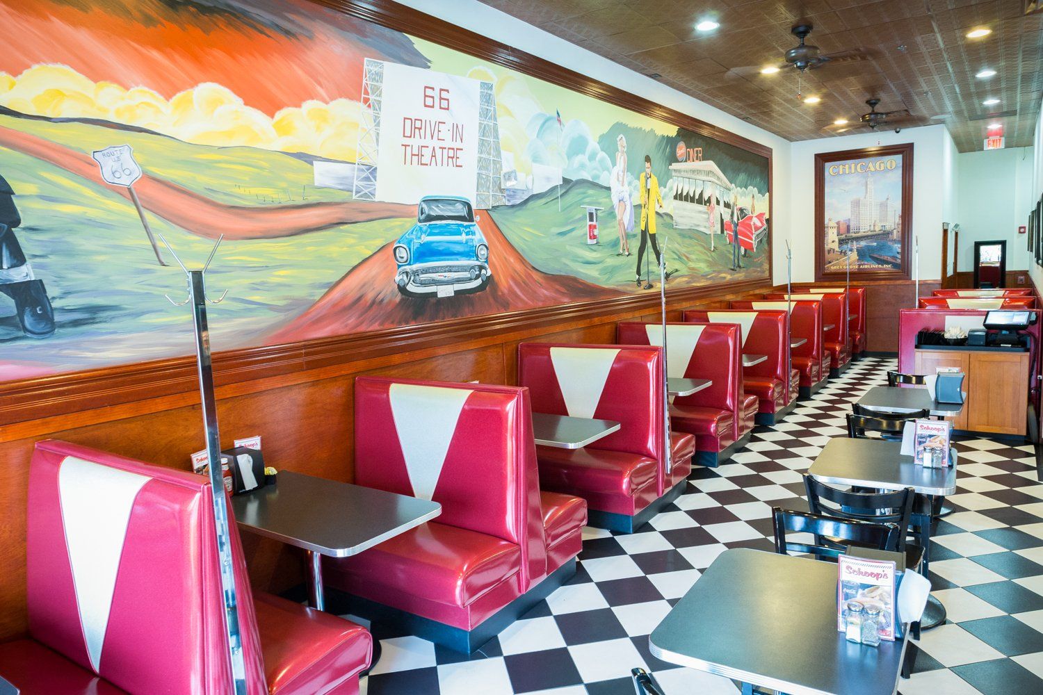 A diner with red and white booths and tables and a mural on the wall.