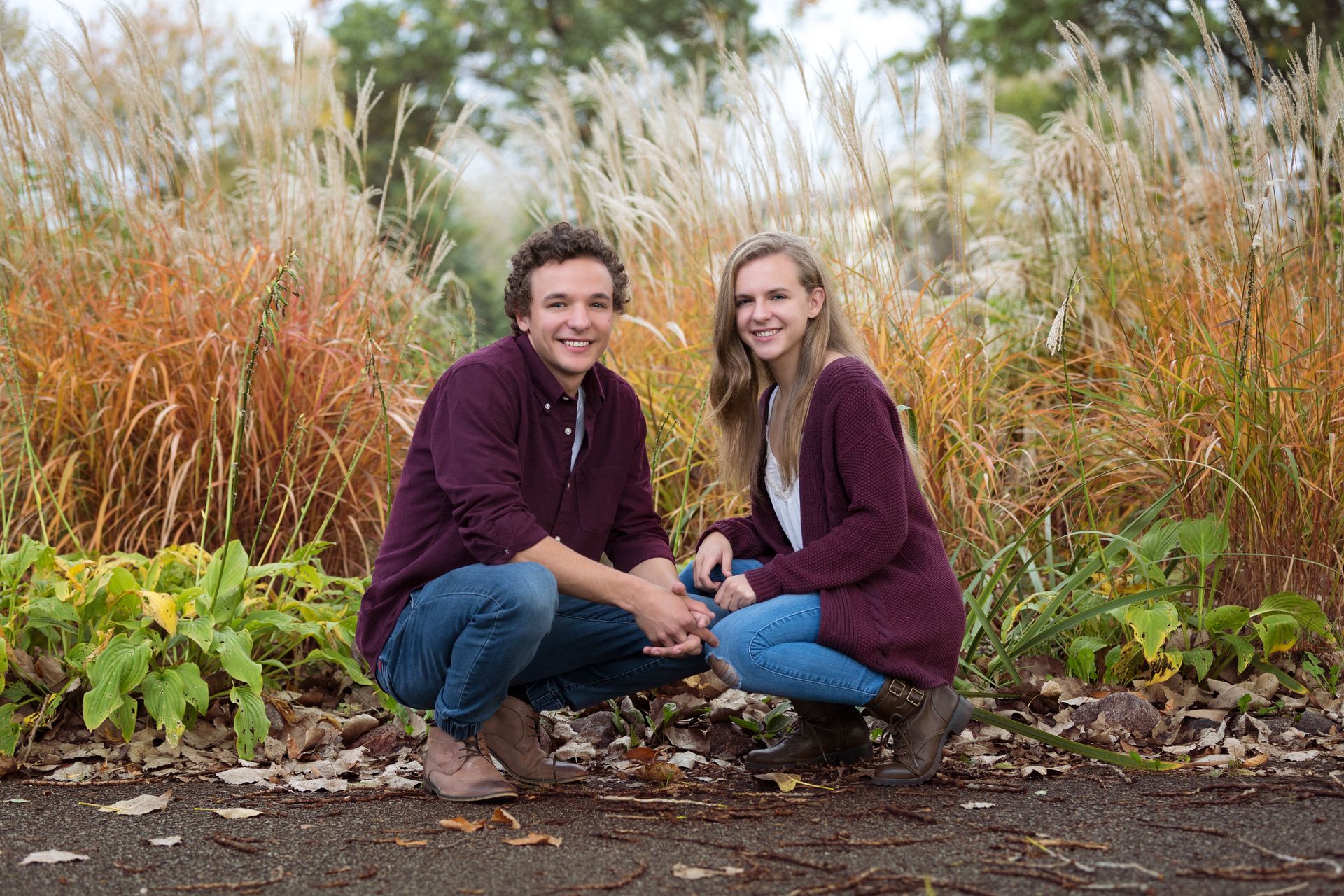 A man and a woman are squatting down in front of a field of tall grass.