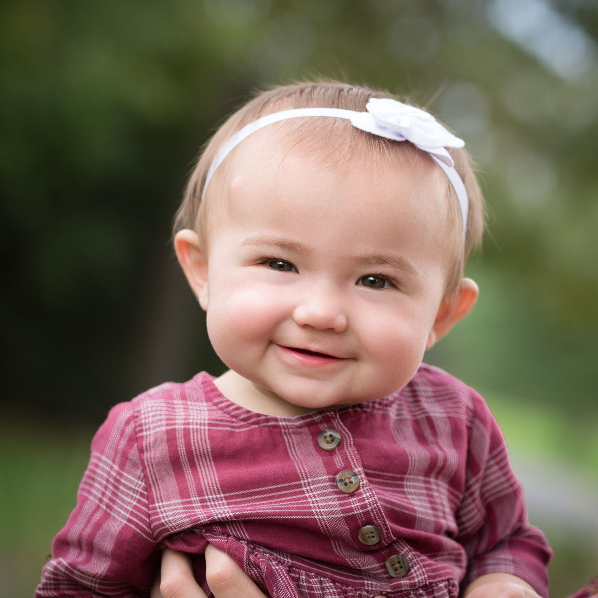 A baby girl wearing a headband is smiling for the camera.