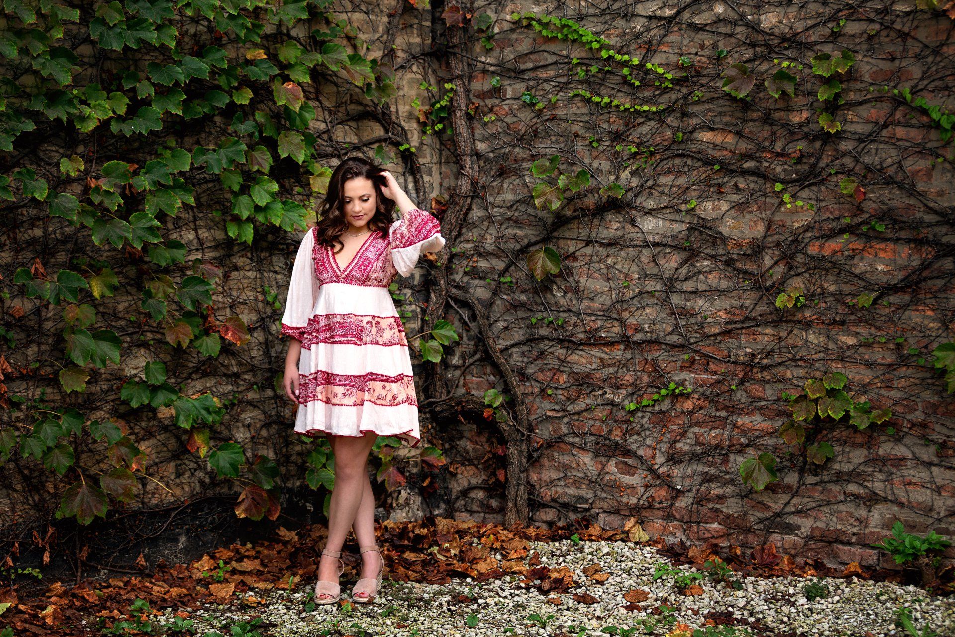 A woman in a pink and white dress is standing in front of a brick wall.