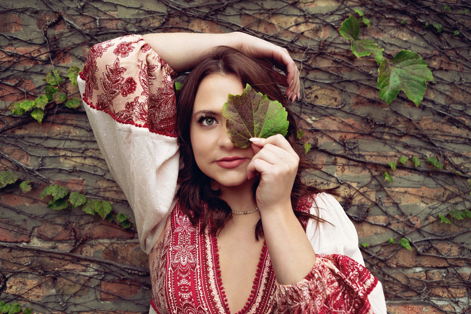A woman in a red and white dress is holding a leaf in front of her face.