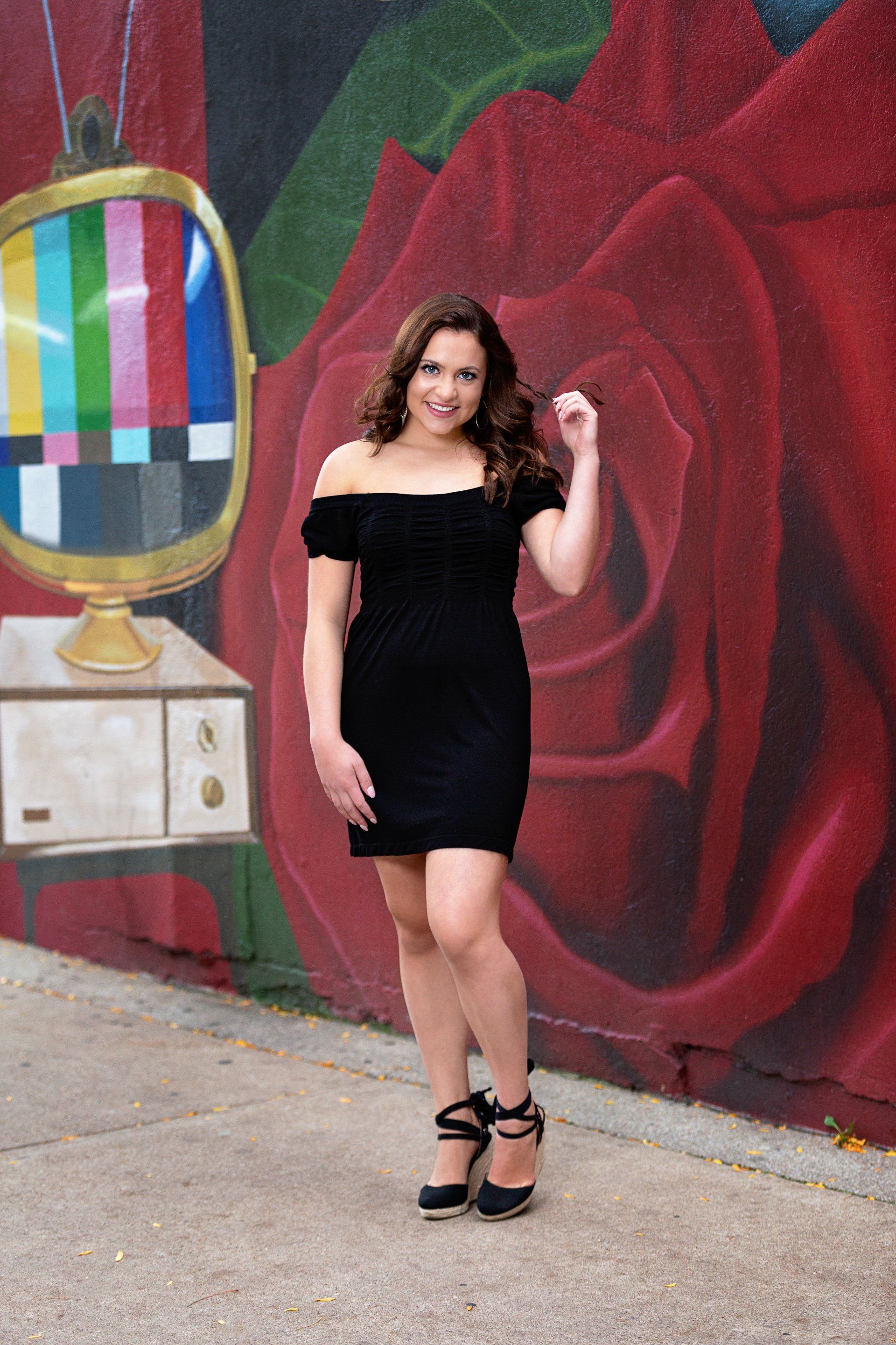 A woman in a black dress is standing in front of a mural on a wall.