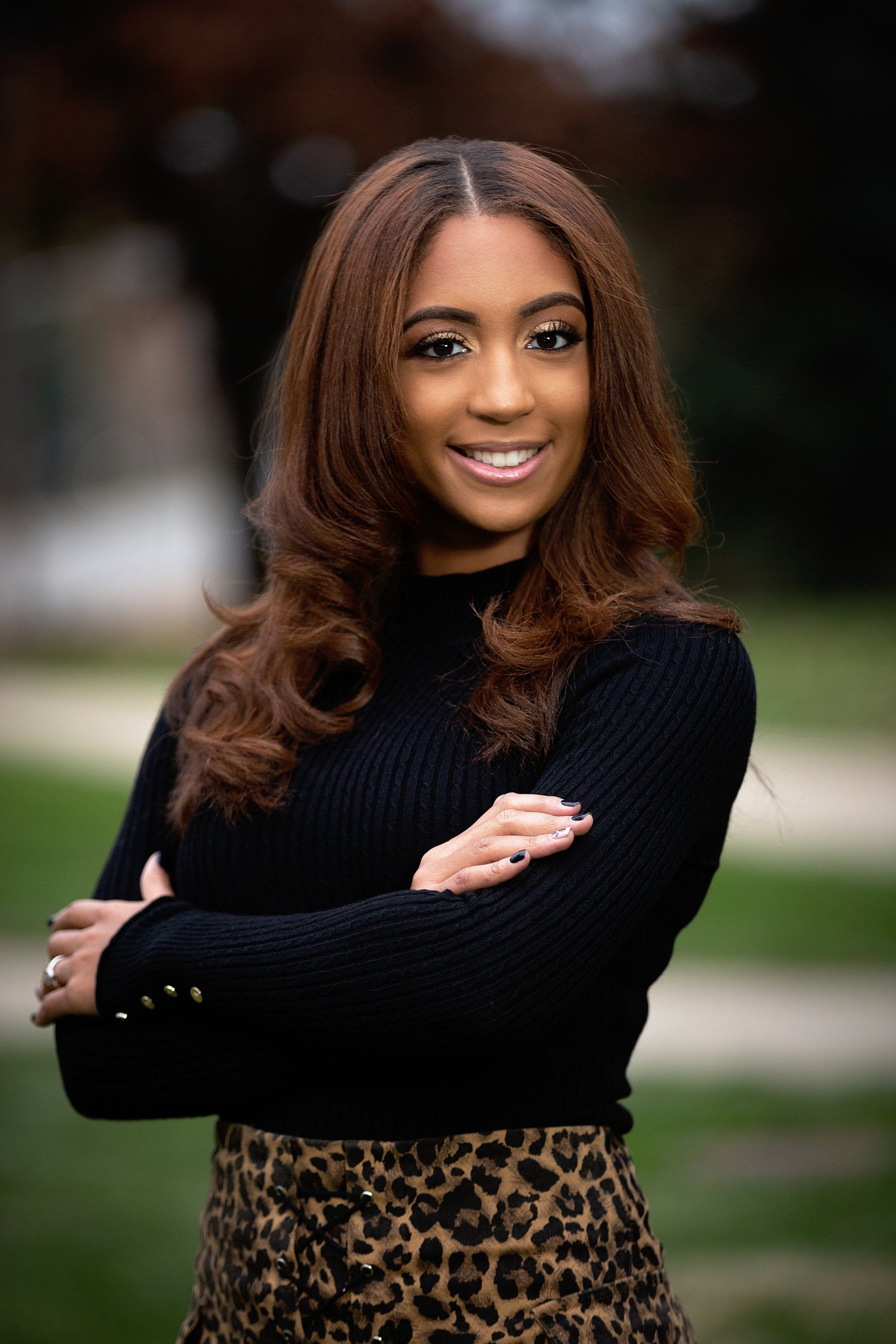 A woman in a black sweater and leopard print skirt is posing for a picture with her arms crossed.