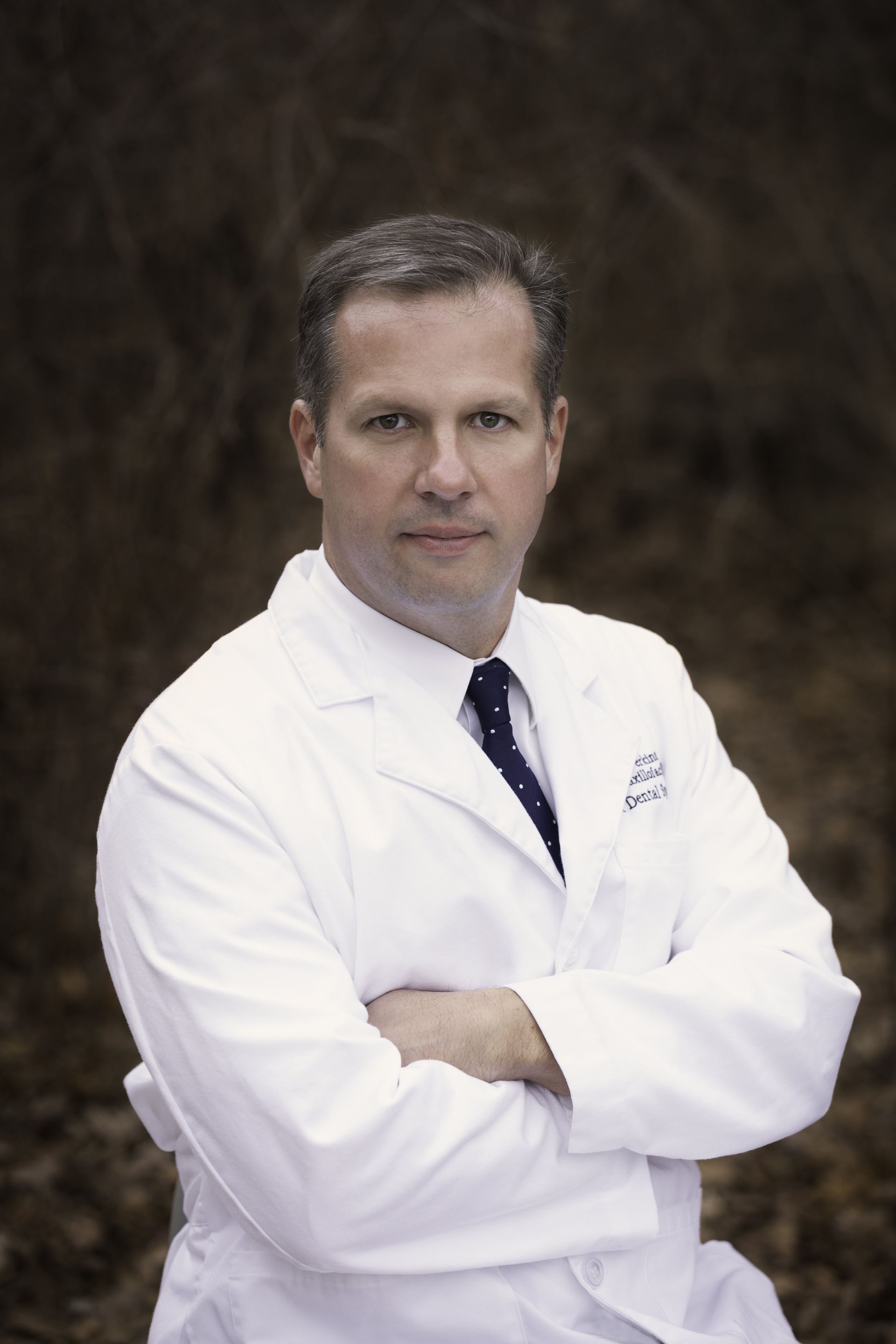 A man in a white coat and tie is standing with his arms crossed.
