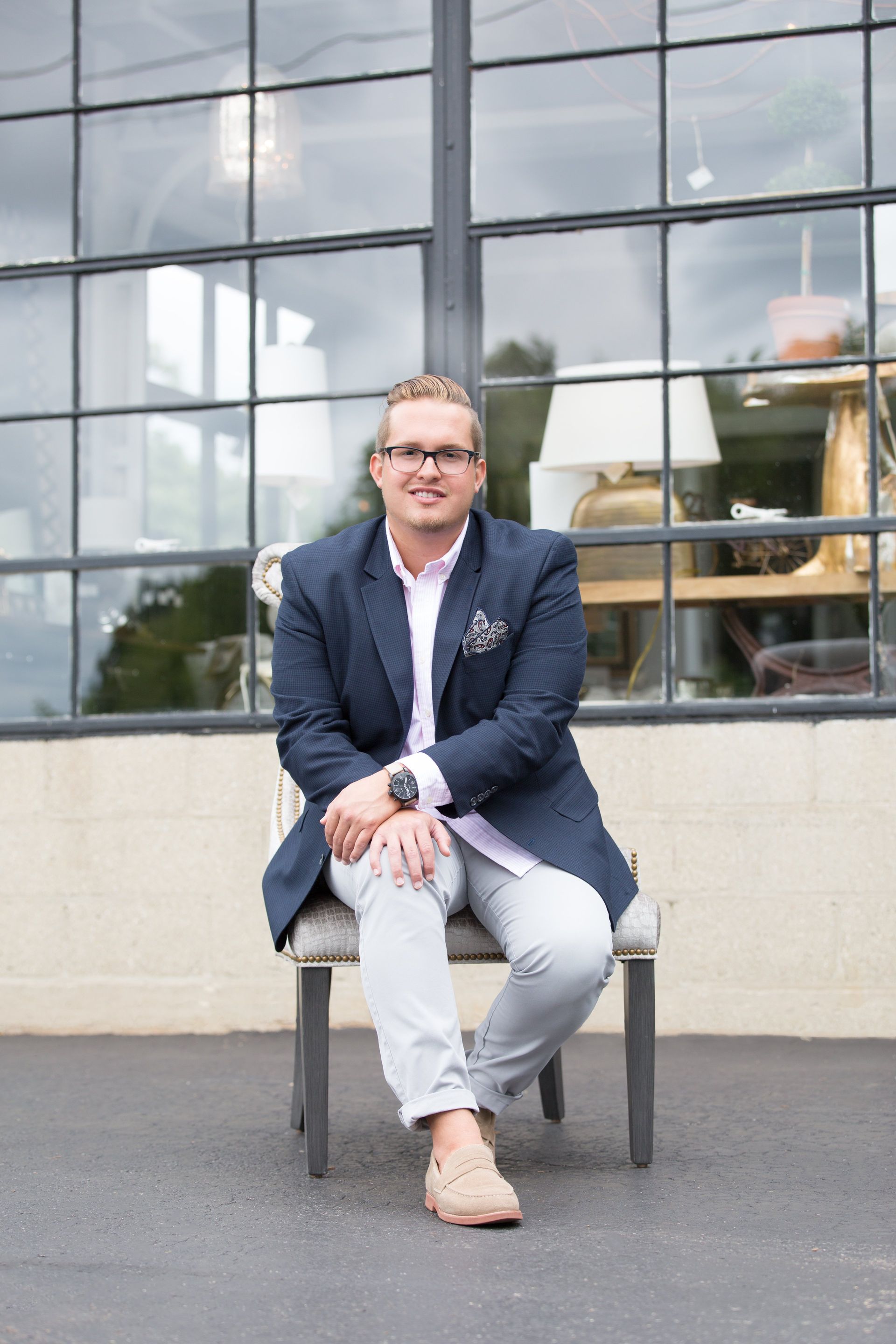 A man in a suit is sitting on a chair in front of a window.