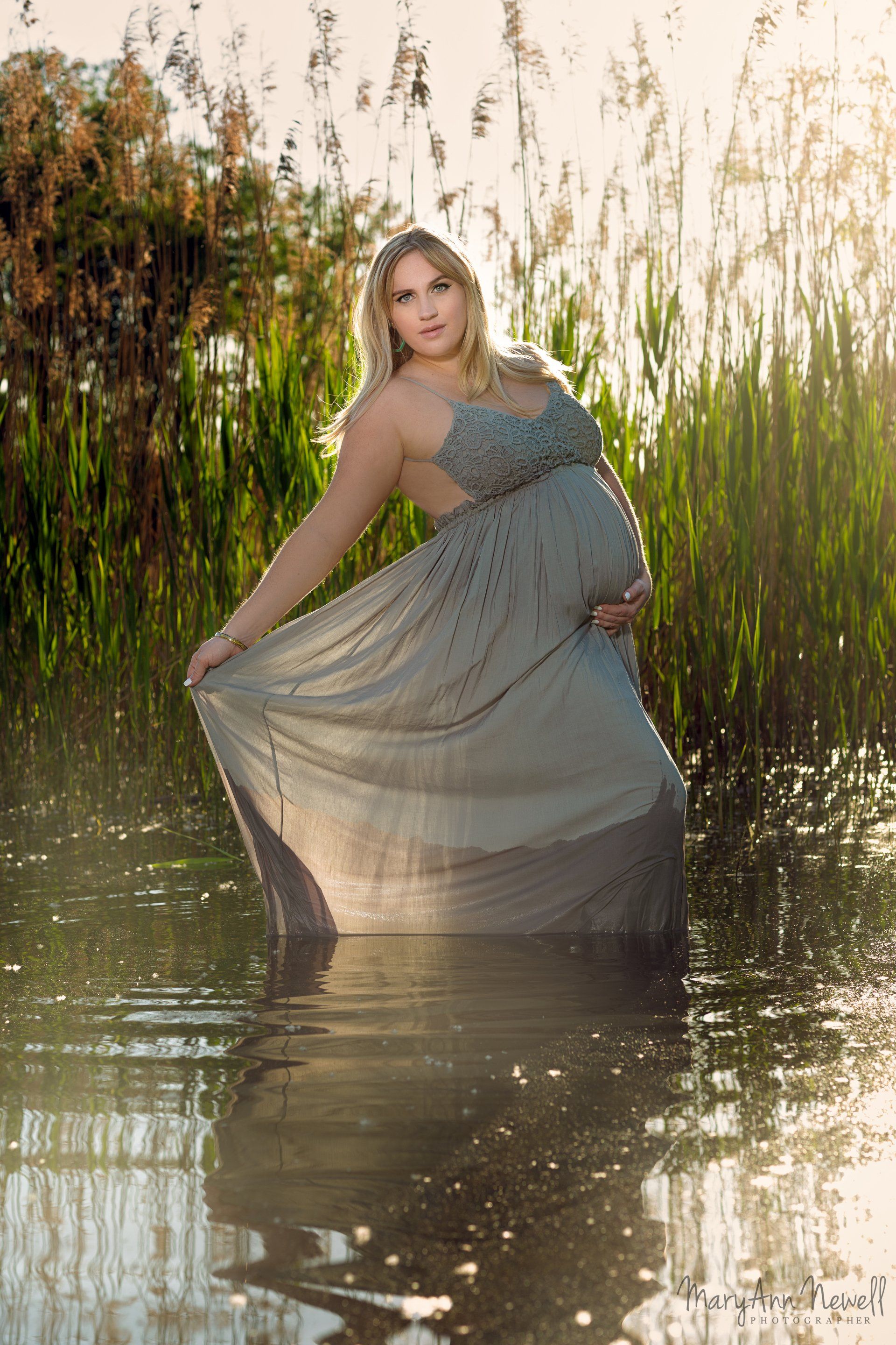 A pregnant woman in a long dress is standing in the water.
