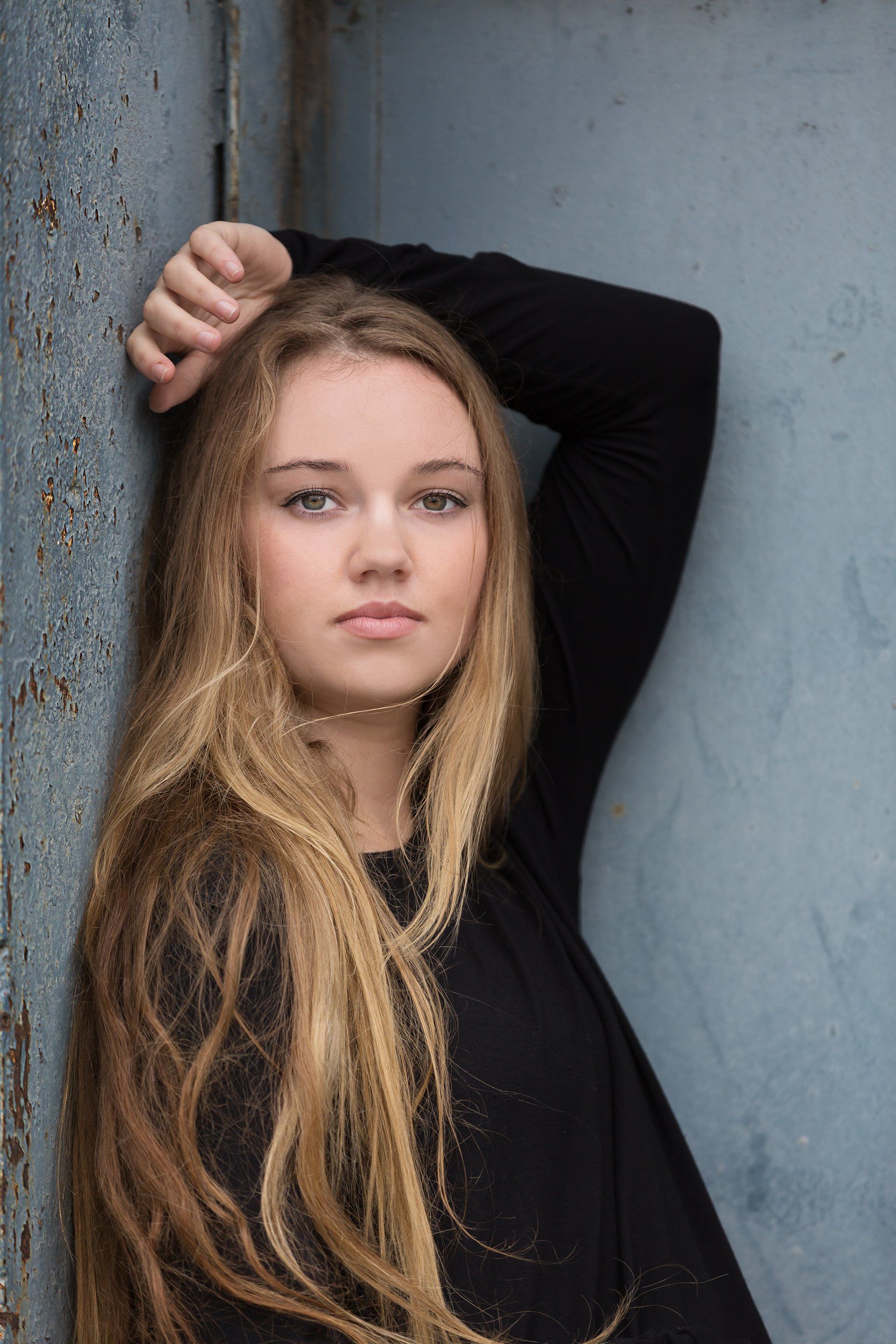 A young woman with long blonde hair is leaning against a wall.