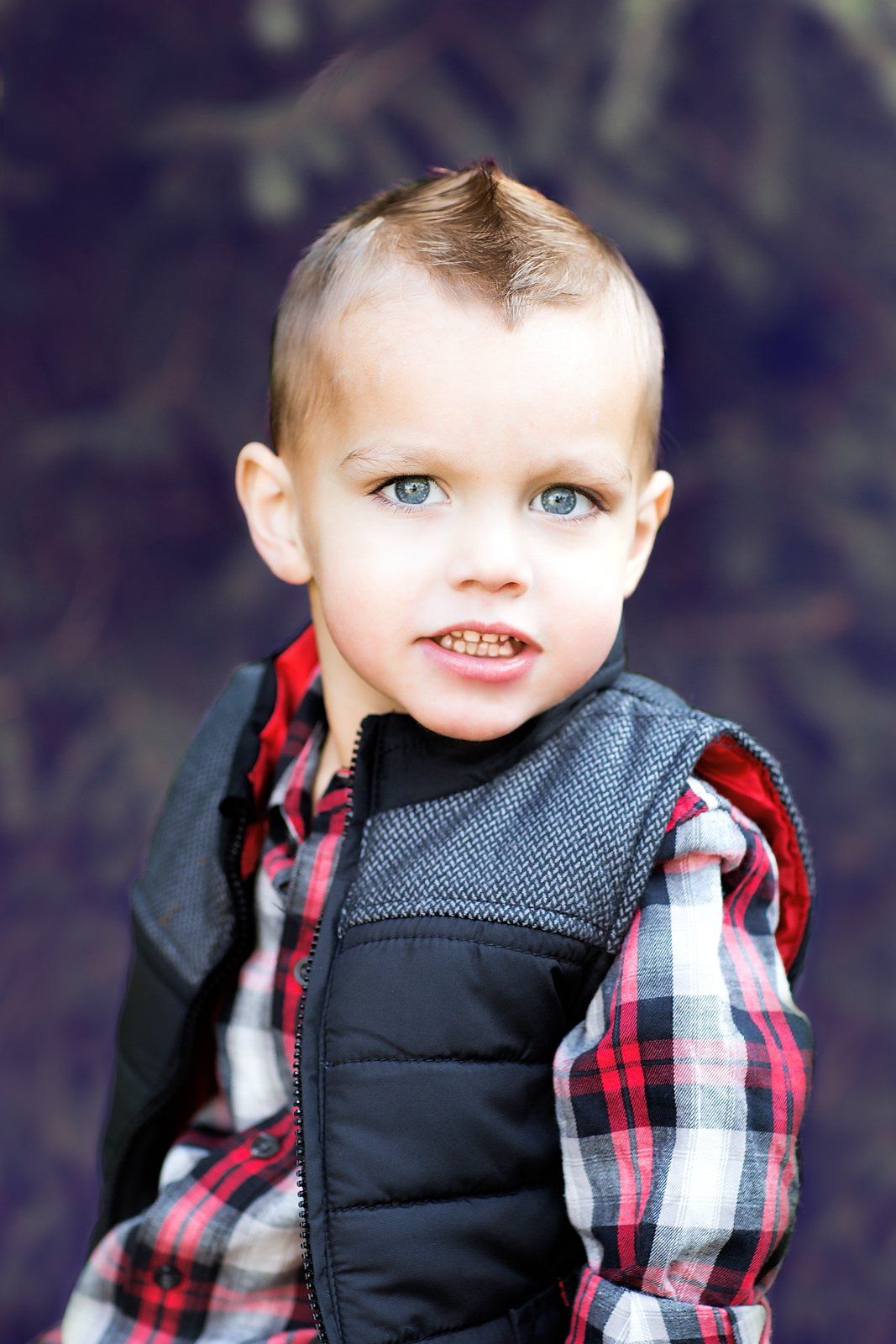 A young boy with a mohawk is wearing a plaid shirt and a black vest.