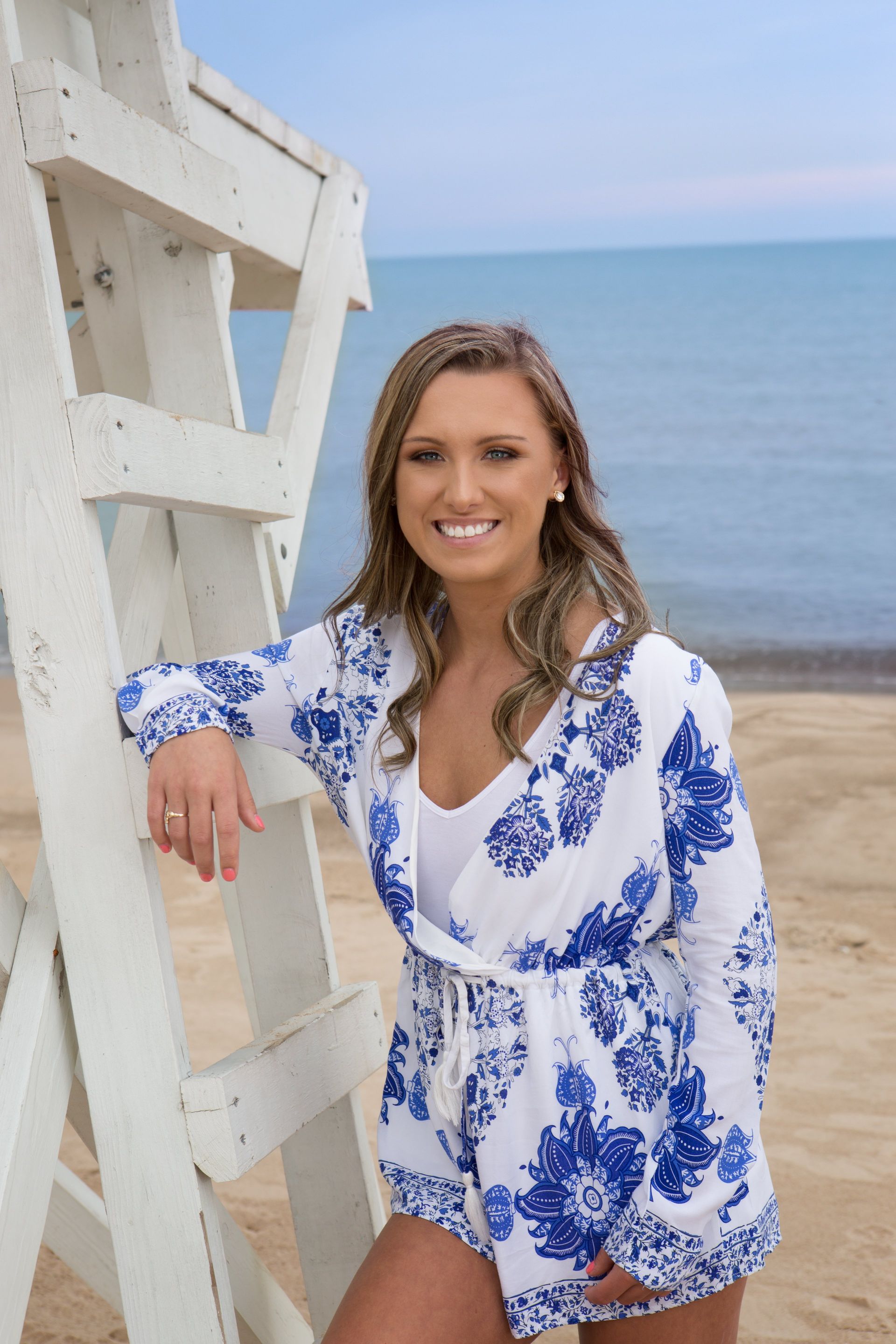 A woman is standing next to a lifeguard tower on the beach.