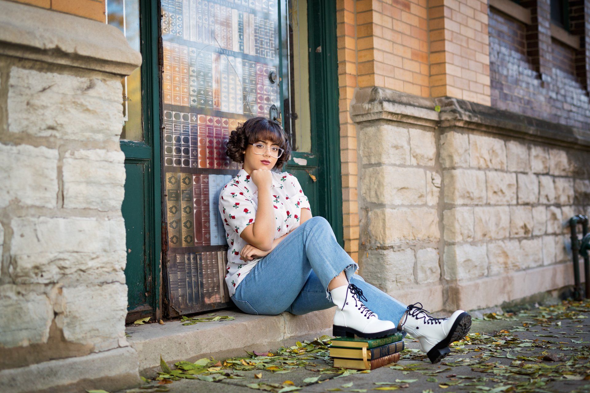 A woman is sitting on the steps of a building next to a stack of books.