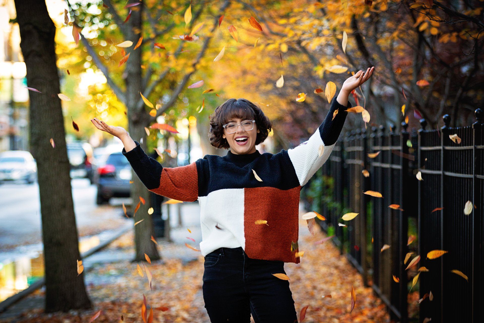 A woman in a sweater is throwing leaves in the air.