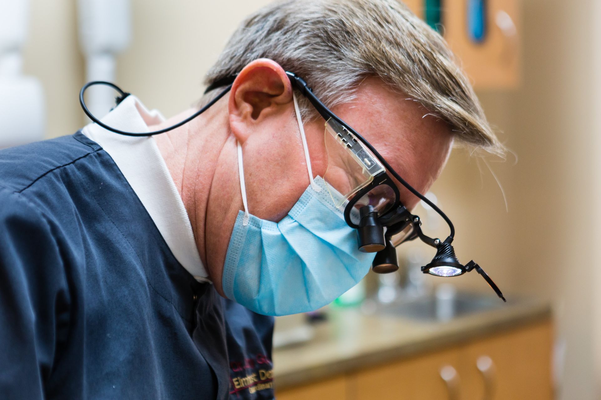 A dentist wearing a mask and magnifying glasses is examining a patient 's teeth.