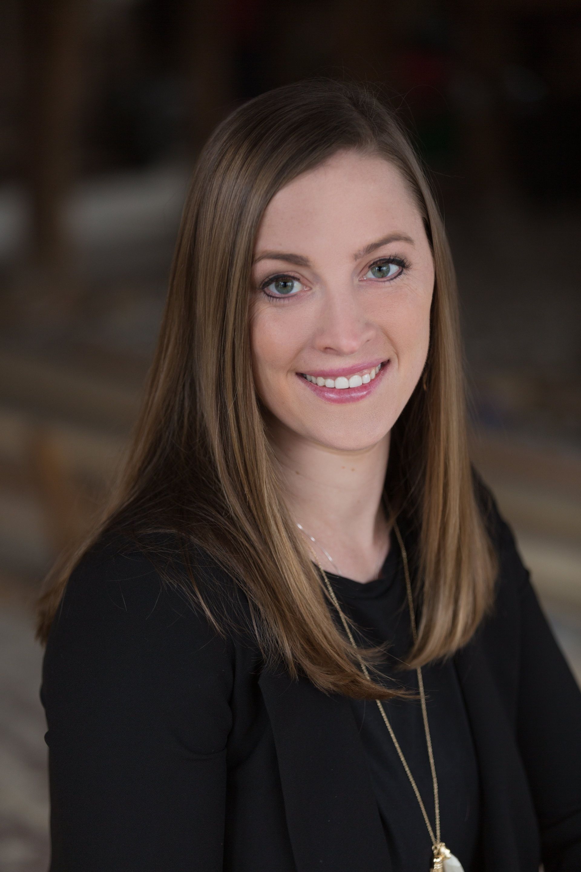 A woman wearing a black shirt and a necklace is smiling for the camera.