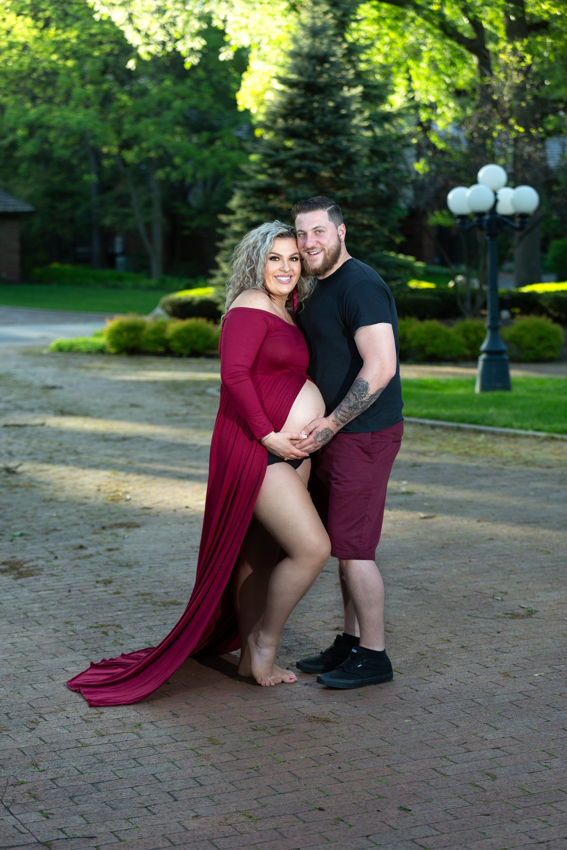 A man and a pregnant woman are posing for a picture in a park.