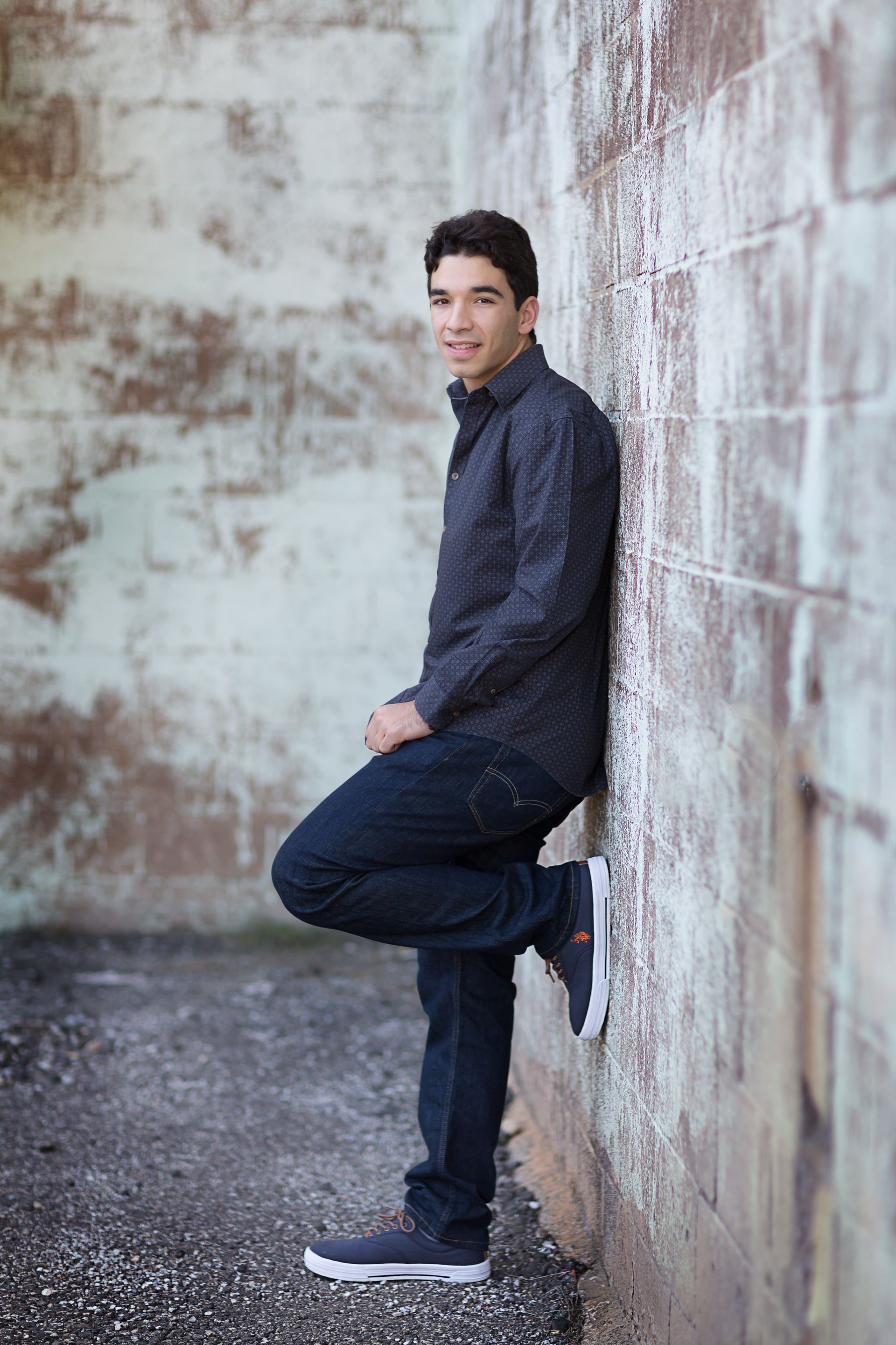 A young man is leaning against a brick wall.