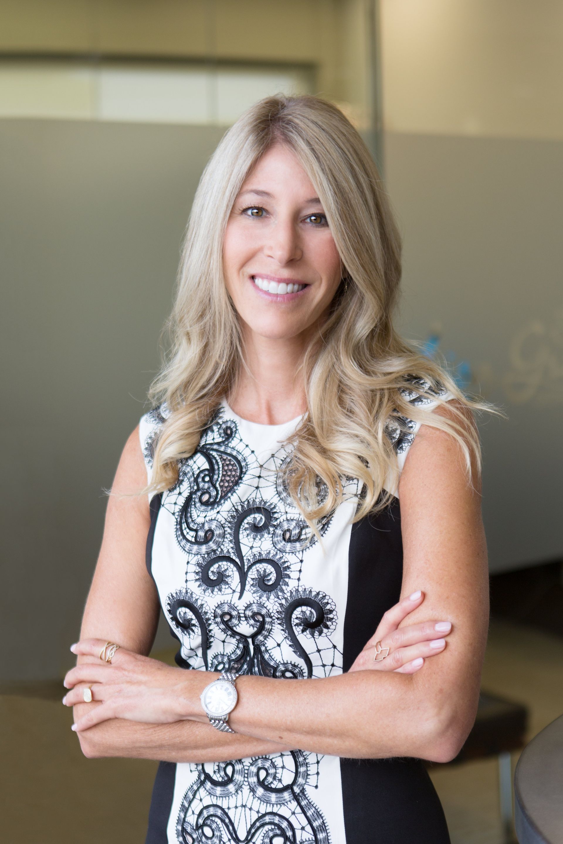 A woman in a black and white dress is standing with her arms crossed and smiling.