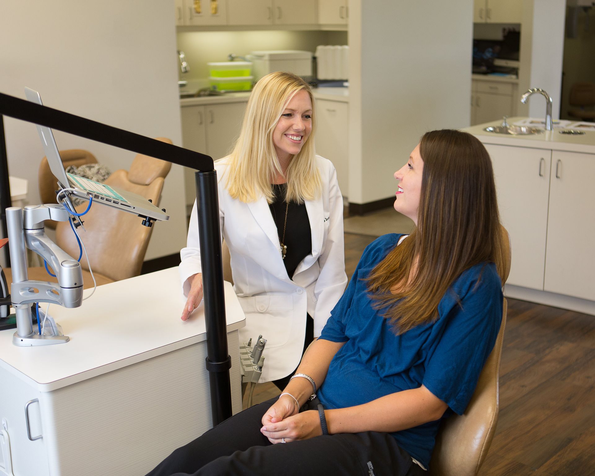 A woman is sitting in a dental chair talking to a dentist.