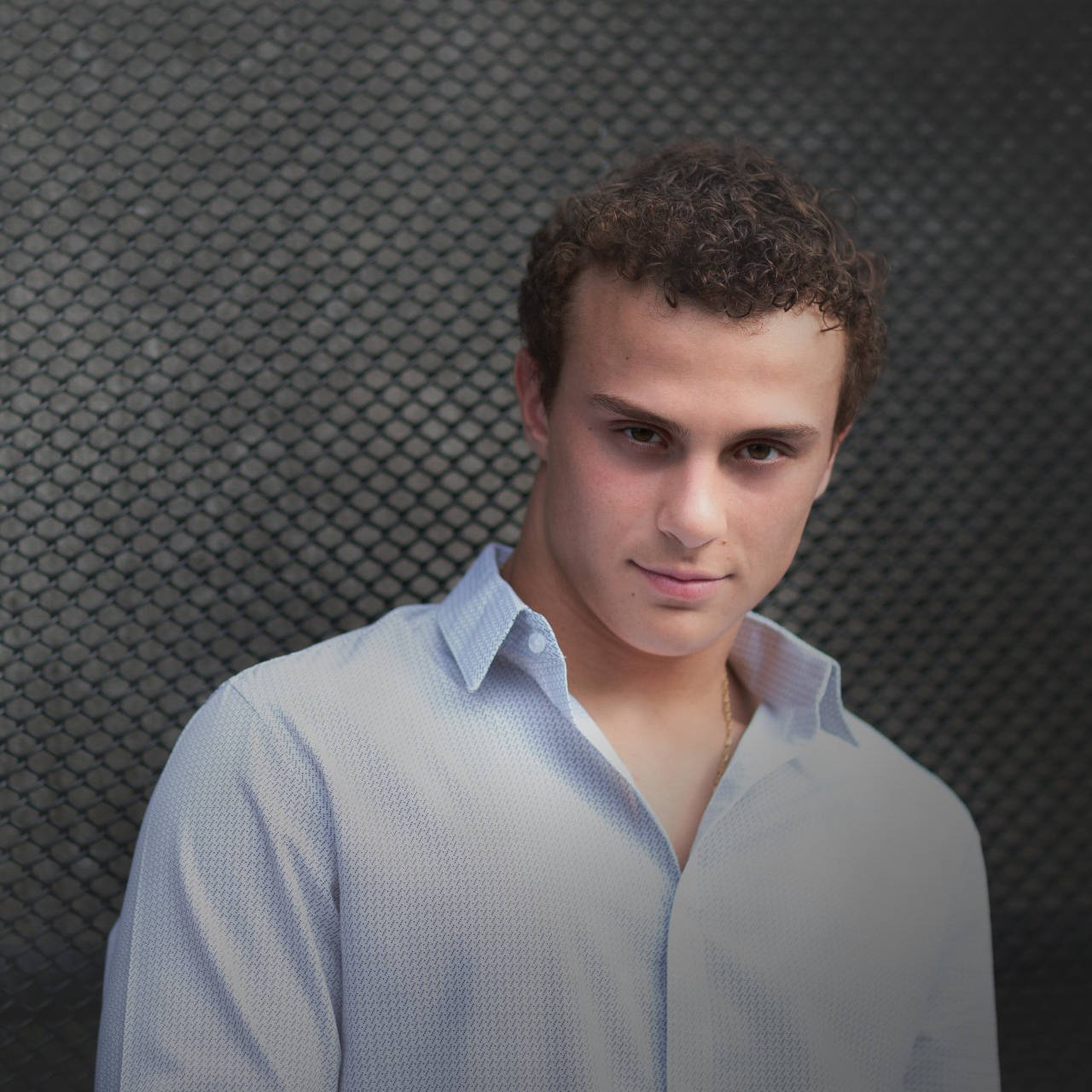 A man in a light blue shirt is standing in front of a black background