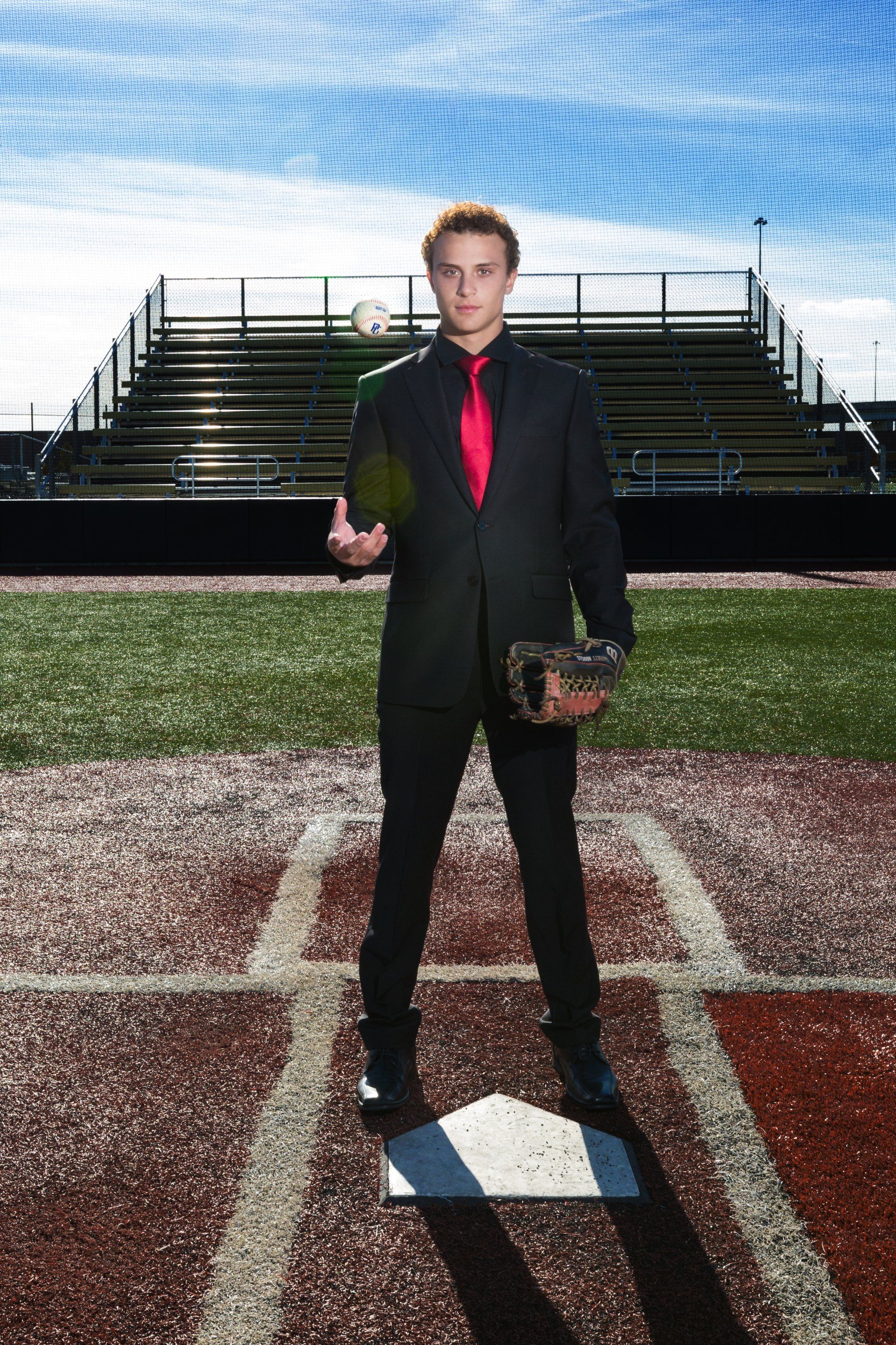 A man in a suit and tie is standing on a baseball field holding a glove.