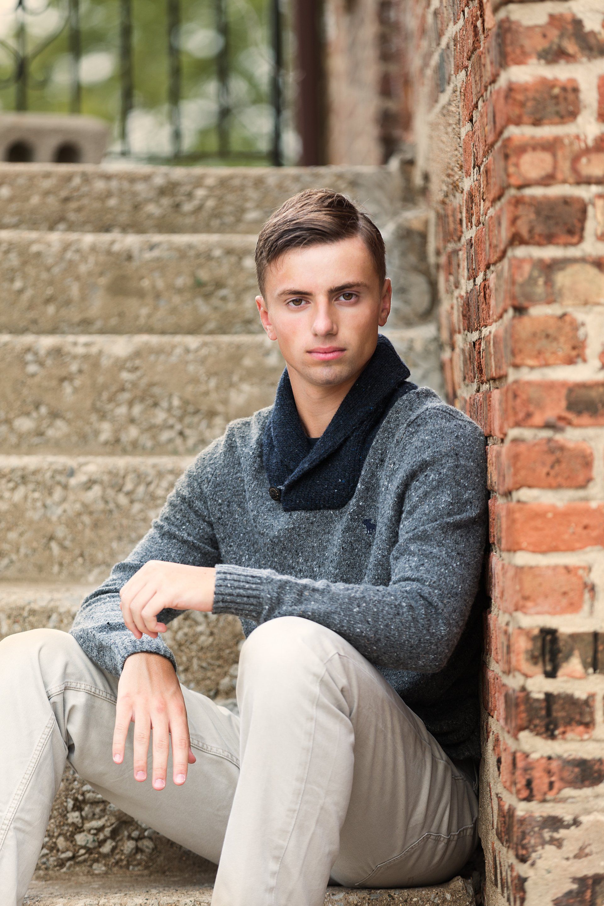 A young man is sitting on a set of stairs leaning against a brick wall.
