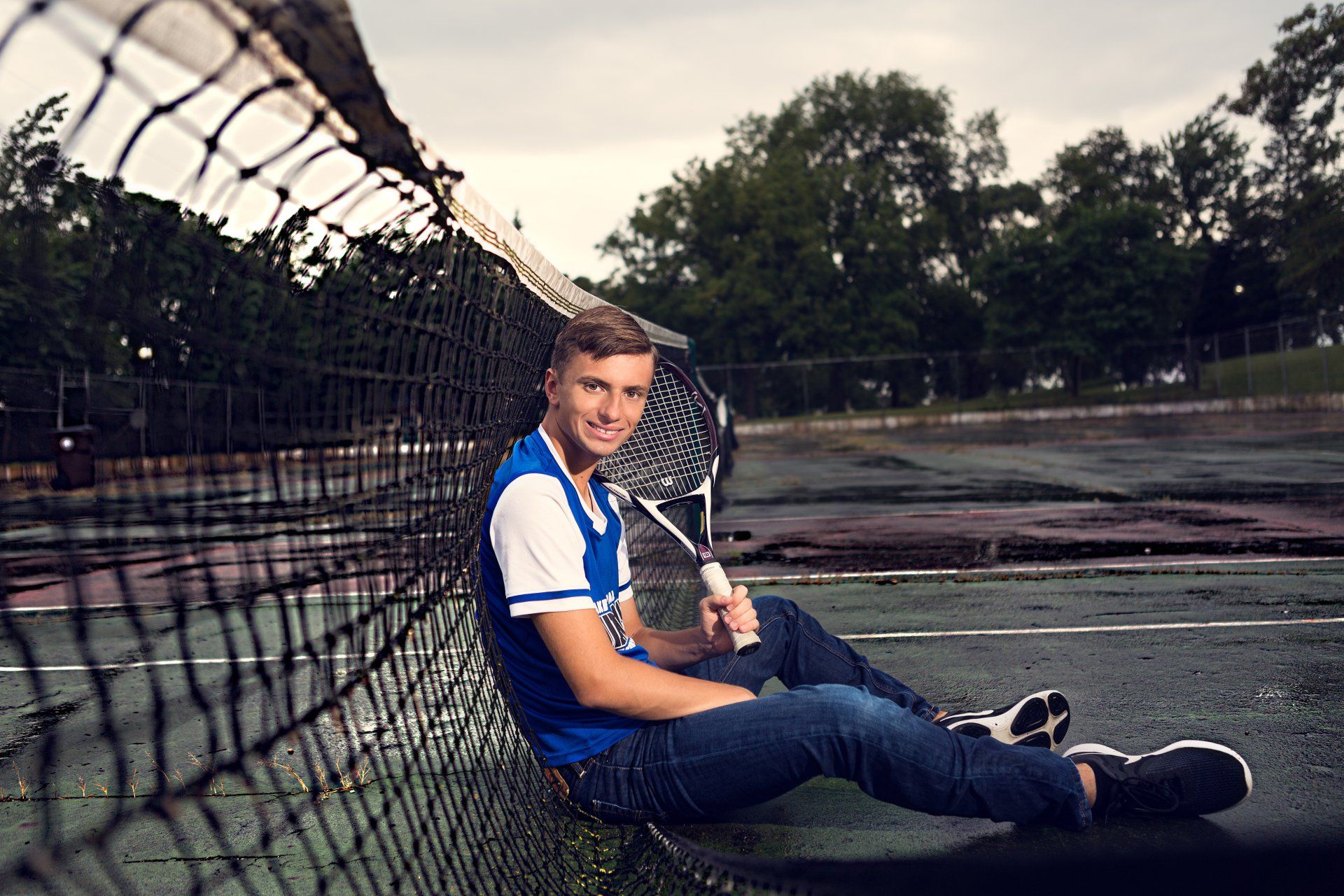 A young man is sitting on a tennis court holding a tennis racquet.