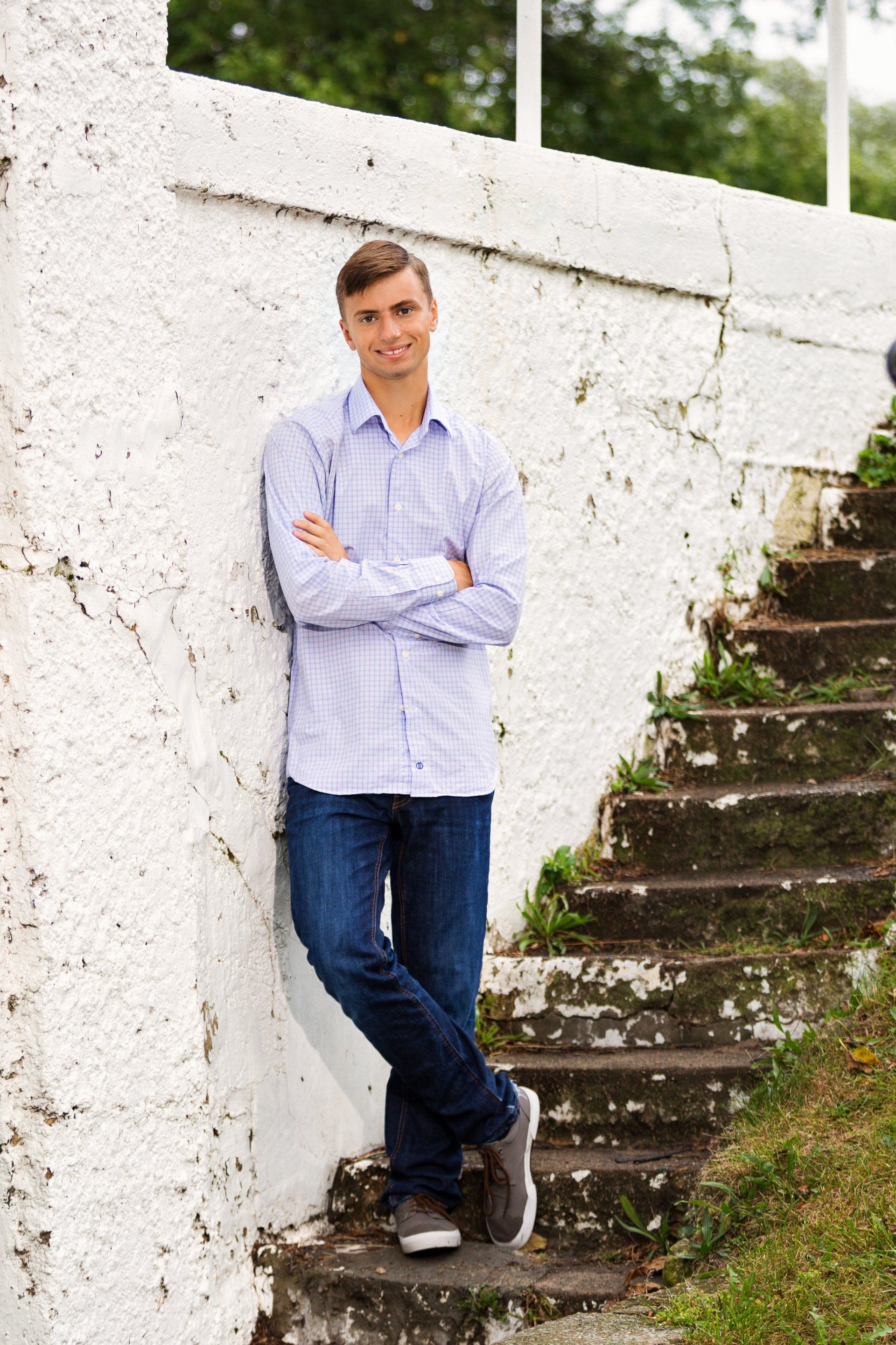 A young man is leaning against a white wall and stairs.