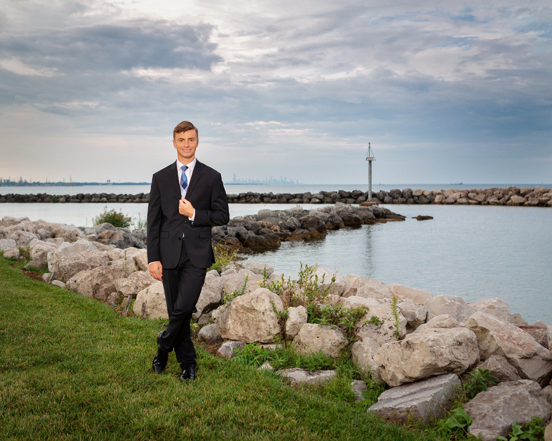 A man in a suit and tie is standing in front of a body of water.
