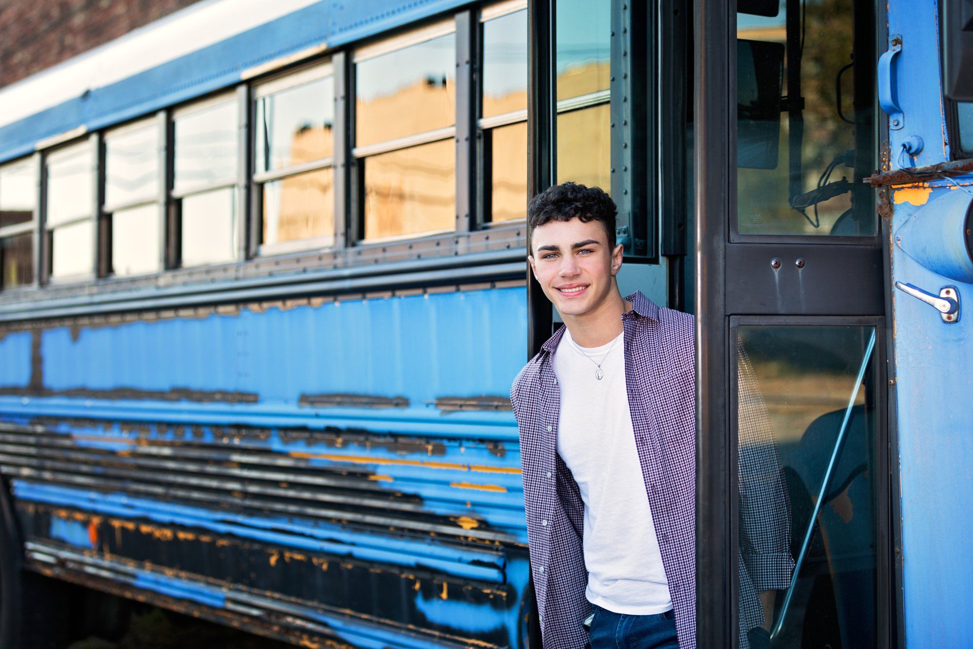A young man is standing next to a blue school bus.