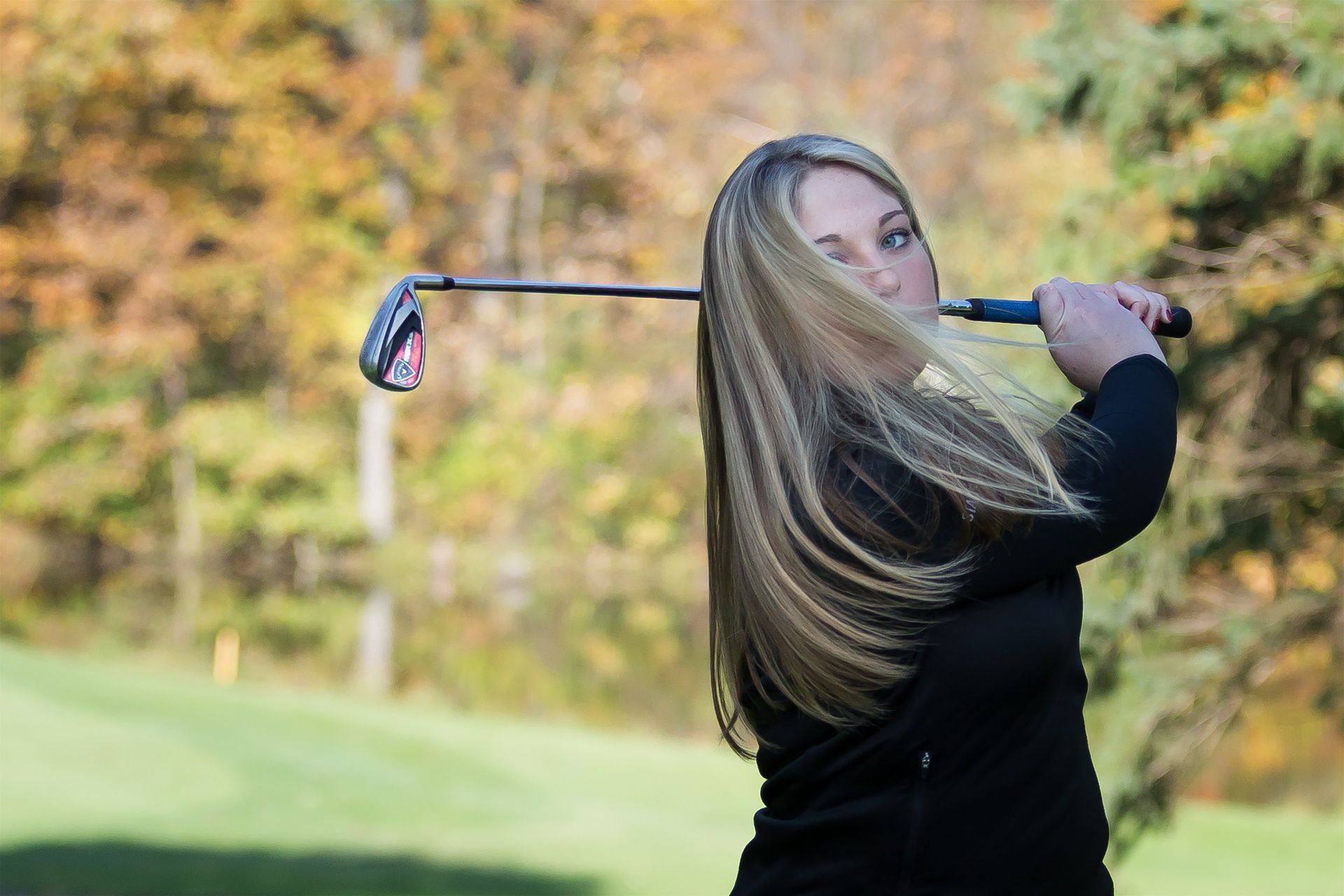 A woman is swinging a golf club on a golf course.
