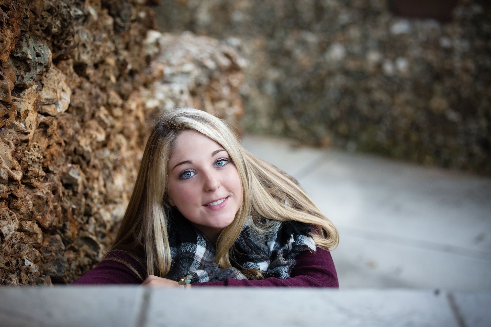 A young woman is leaning against a rock wall and smiling.