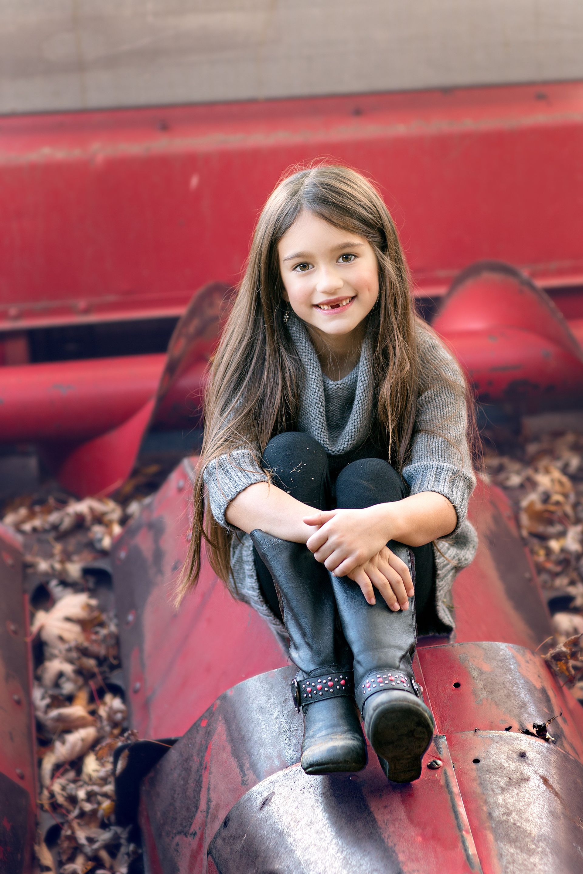 A little girl is sitting on top of a red pipe.