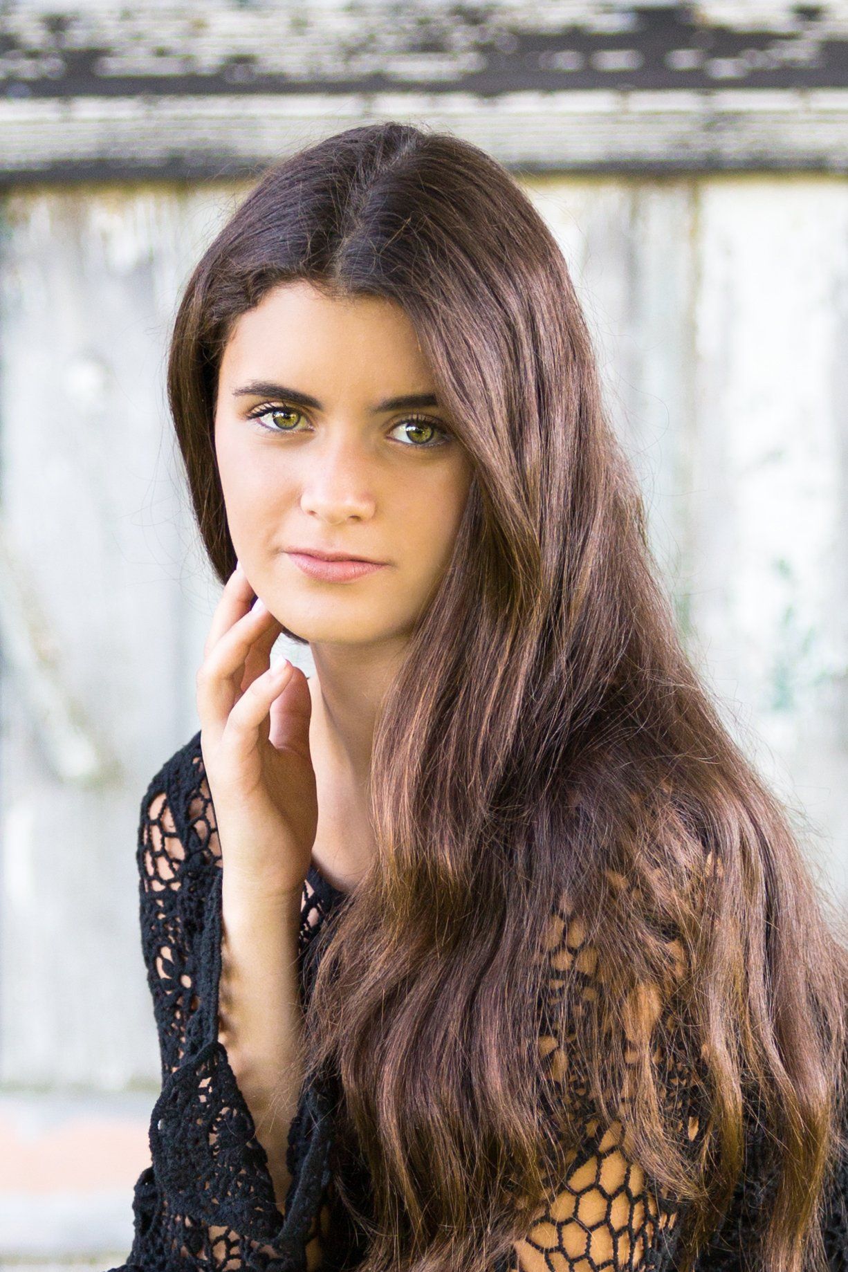 A young woman with long brown hair and green eyes is wearing a black lace top.