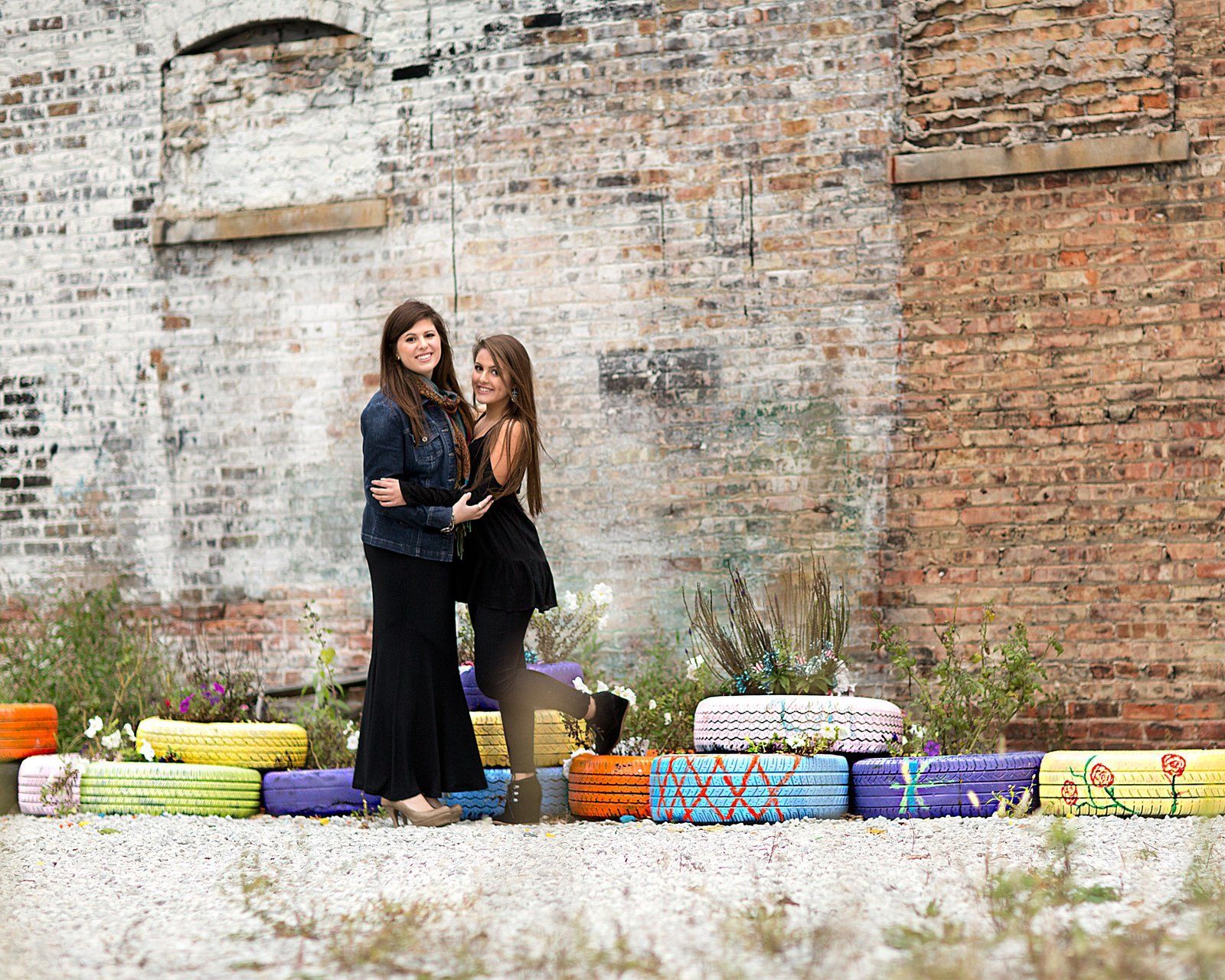 Two women are standing next to each other in front of a brick wall.